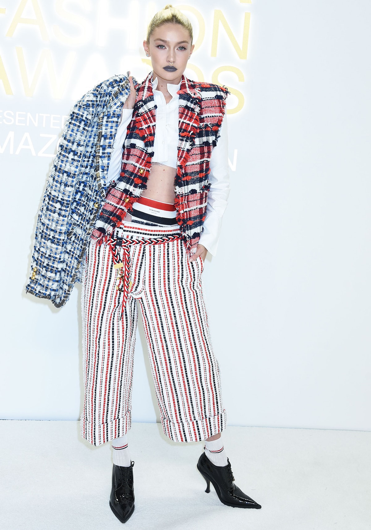 Gigi Hadid leans into glam-punk tailoring in a multi-patterned Thom Browne menswear look, grounding the statement ensemble with sharp black pointed-toe heeled brogues