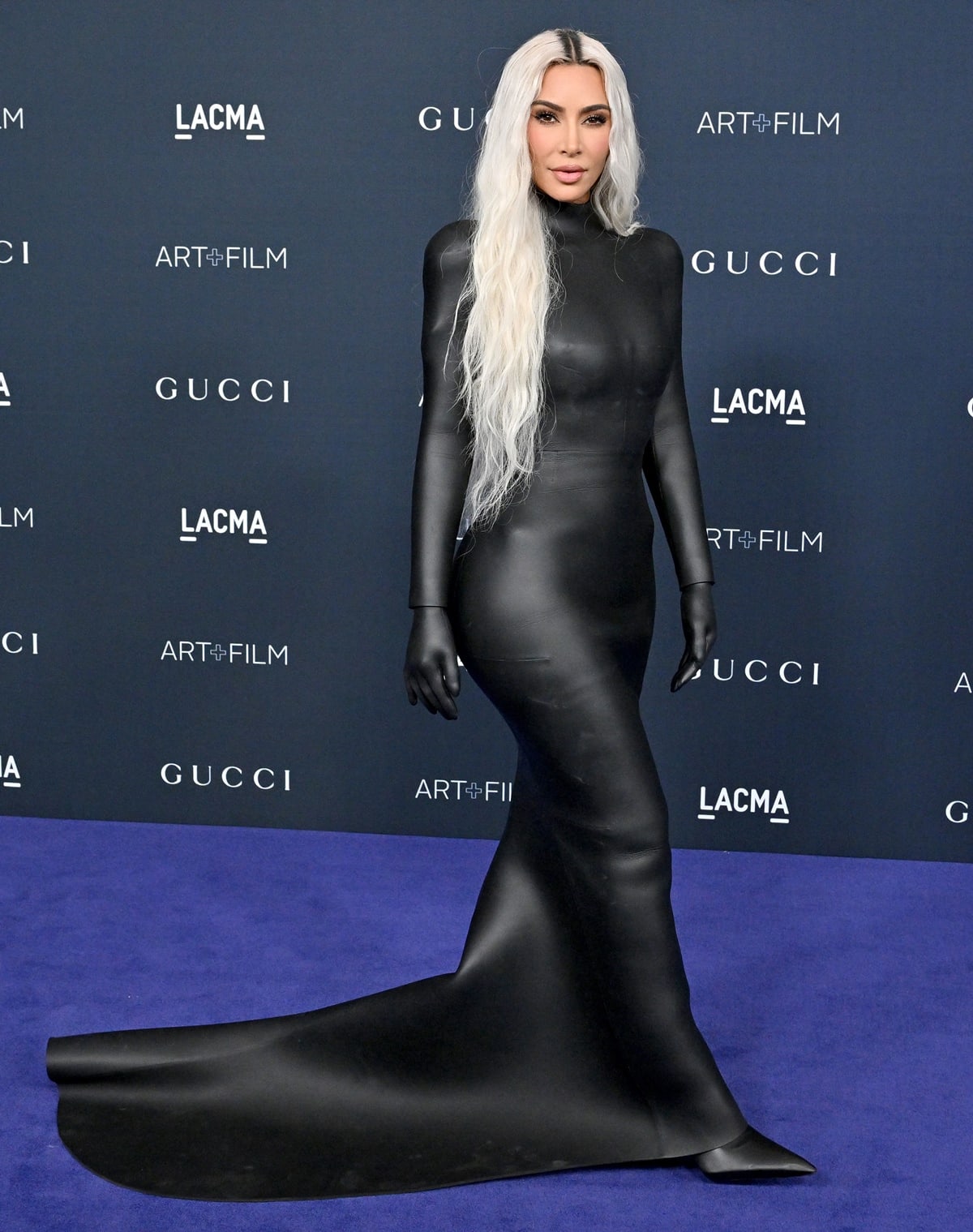 Kim Kardashian stuns in a fitted black Balenciaga gown with built-in gloves, finishing the look with matching black vinyl pointed-toe Balenciaga boots that extend the head-to-toe silhouette