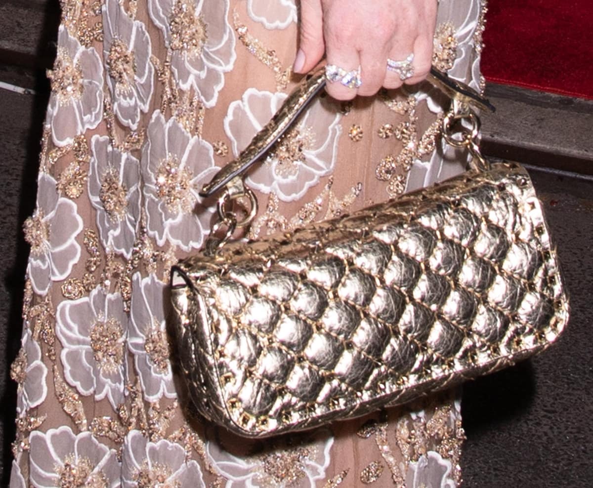Lindsay Lohan carries a metallic Valentino Garavani Rockstud Spike bag in quilted lambskin, its glossy gold finish and signature stud detailing echoing the shimmer of her sequined floral lace gown