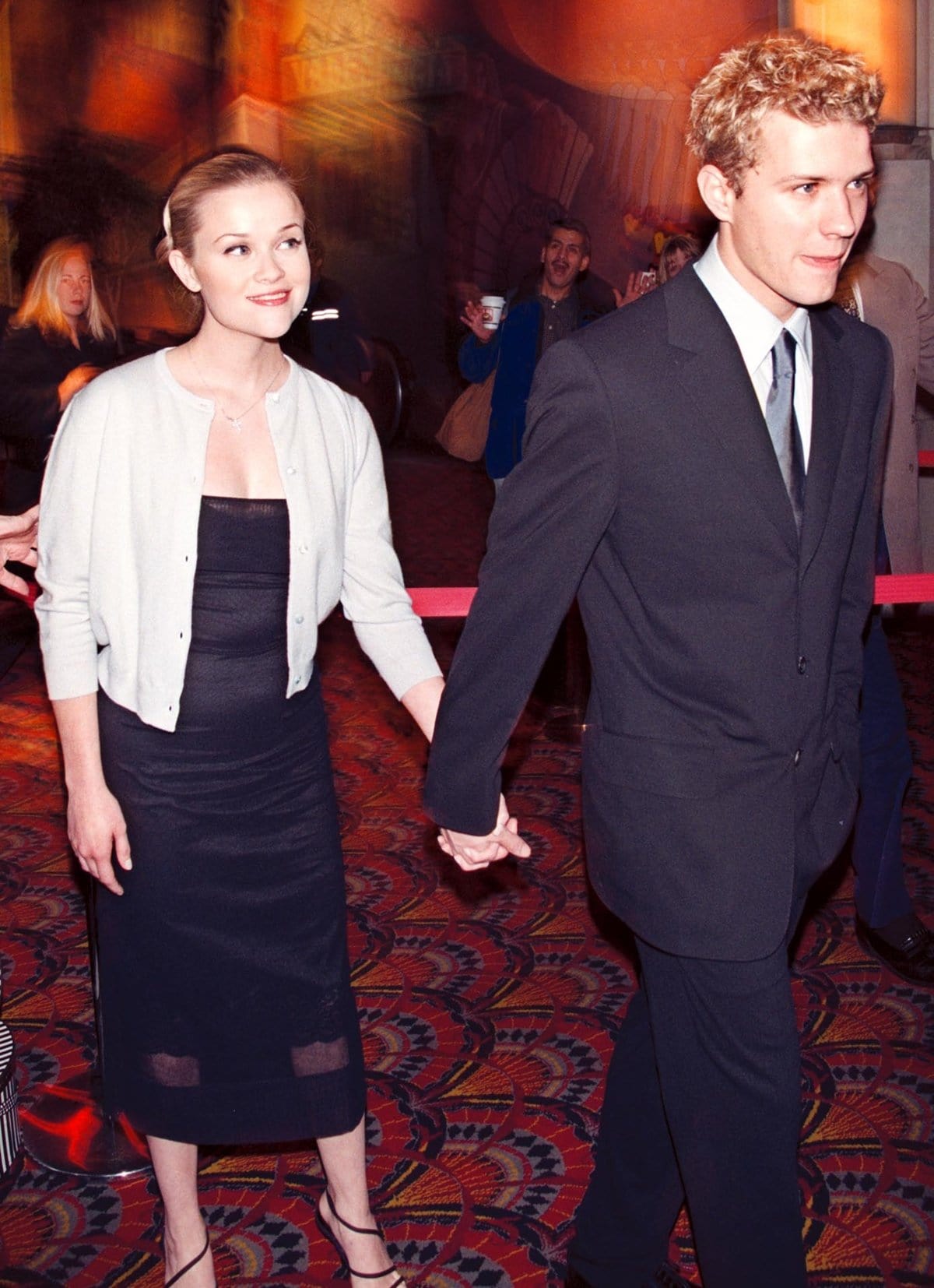 Reese Witherspoon keeps it sleek in a fitted black midi dress, soft cardigan, and minimalist strappy sandals, arriving hand-in-hand with Ryan Phillippe at the Cruel Intentions Westwood premiere on February 25, 1999