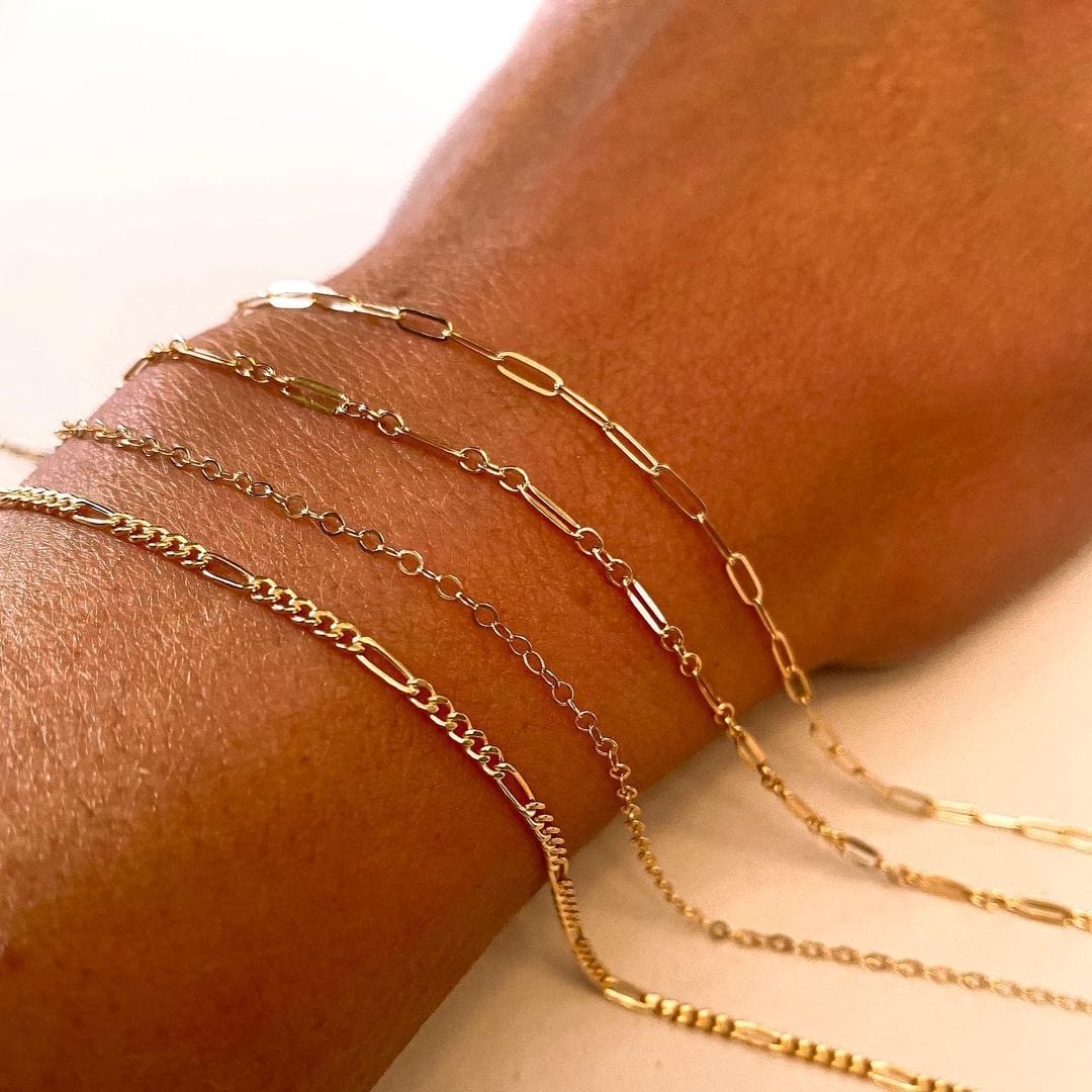 Gold chain bracelets in varying link styles—paperclip, cable, and curb—show the minimalist versatility of permanent jewelry