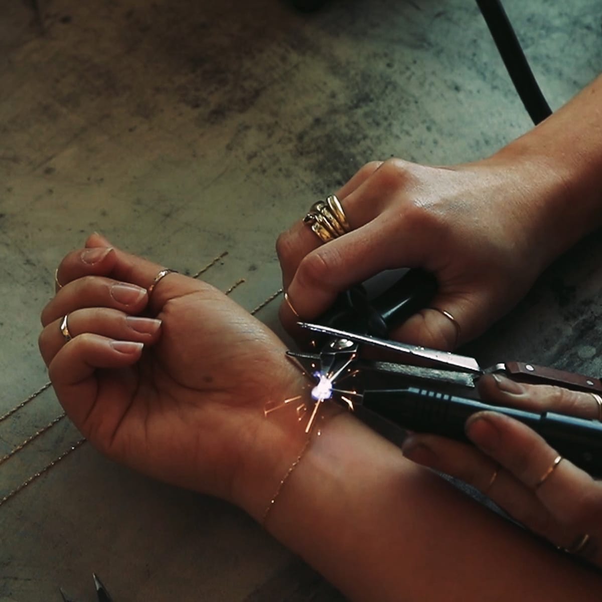 A jeweler uses a precision welder to attach a delicate chain bracelet, creating a seamless piece of permanent jewelry designed to last indefinitely