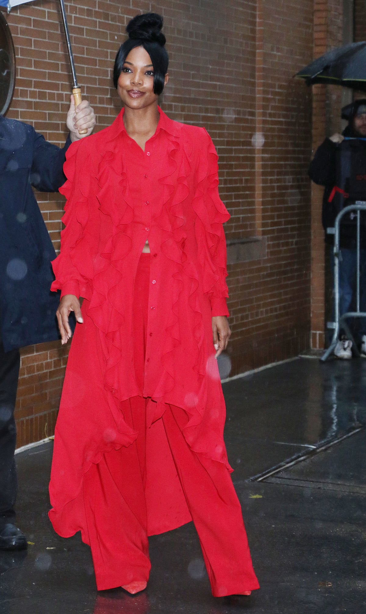 Gabrielle Union makes a striking entrance at The View in a vibrant red ruffled shirtdress layered over matching wide-leg trousers from her NY Company collection, finishing the monochrome look with sharp pointed-toe pumps that subtly peek out beneath the flowing hem