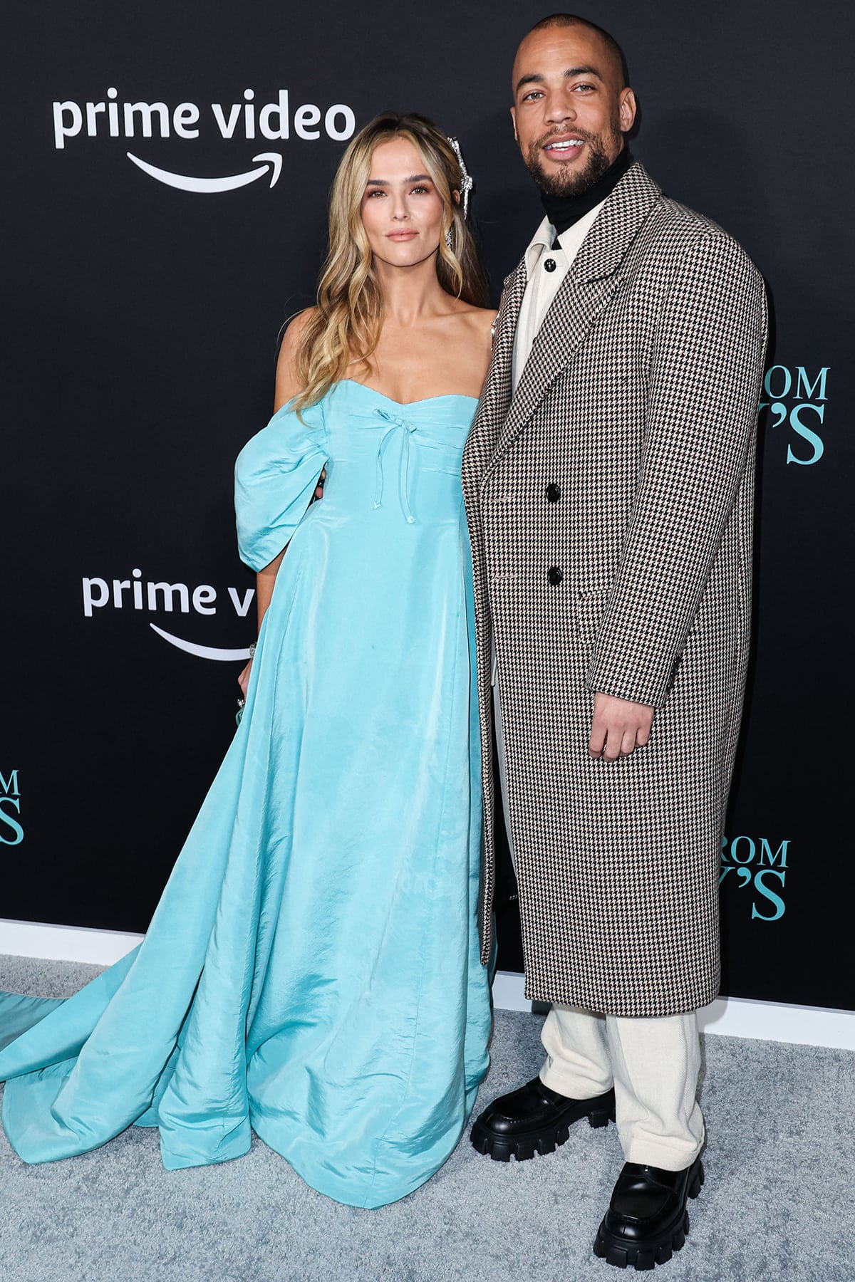 Zoey Deutch looks radiant in a Tiffany-blue Carolina Herrera gown beside co-star Kendrick Sampson, who pairs a houndstooth trench coat with cream tailoring and chunky black platform boots at the Something from Tiffany’s premiere