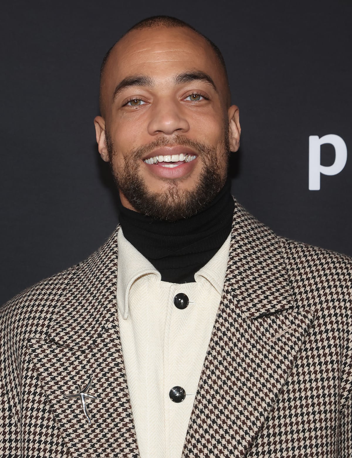 Kendrick Sampson adds subtle shine to his houndstooth coat with a Tiffany Co. Elsa Peretti Starfish brooch and keeps the look refined with a black turtleneck and cream shirt combination