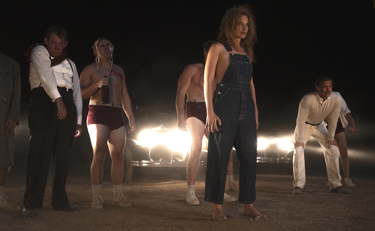 Margot Robbie makes a striking appearance in Babylon, wearing rugged denim overalls barefoot in a tense desert scene