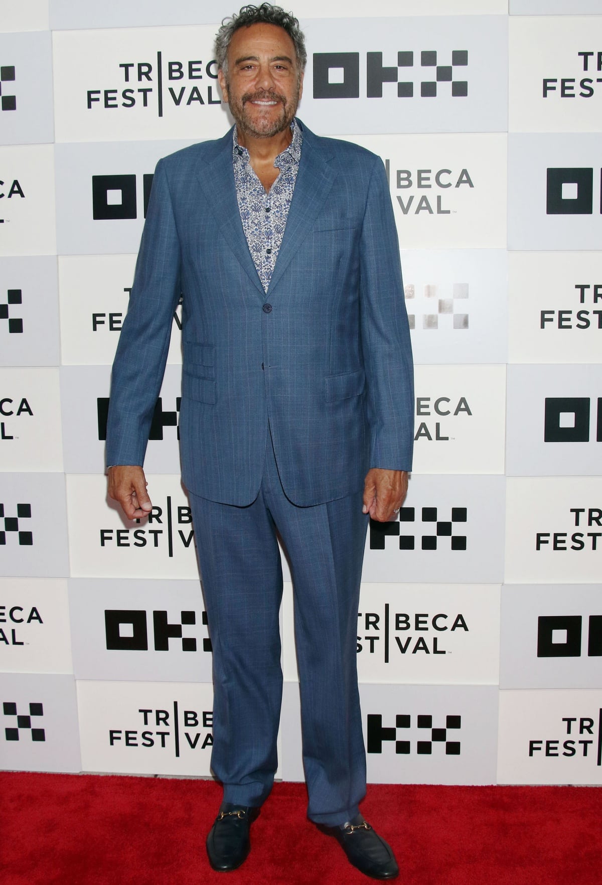 Brad Garrett, towering at 6'8 ⅛" (203.5 cm), brought breezy sophistication to the Cha Cha Real Smooth premiere at the 2022 Tribeca Film Festival in a soft blue plaid suit, floral shirt, and black horsebit loafers that grounded his red carpet look with classic ease