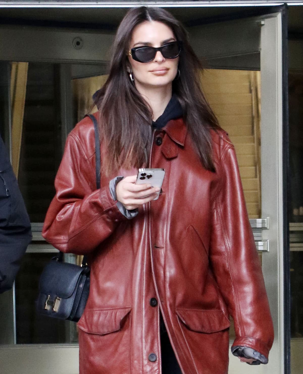 Emily Ratajkowski carries a black Hermes back over her shoulder and hides her eyes behind a pair of Versace by Fendi V1 Fendace sunglasses