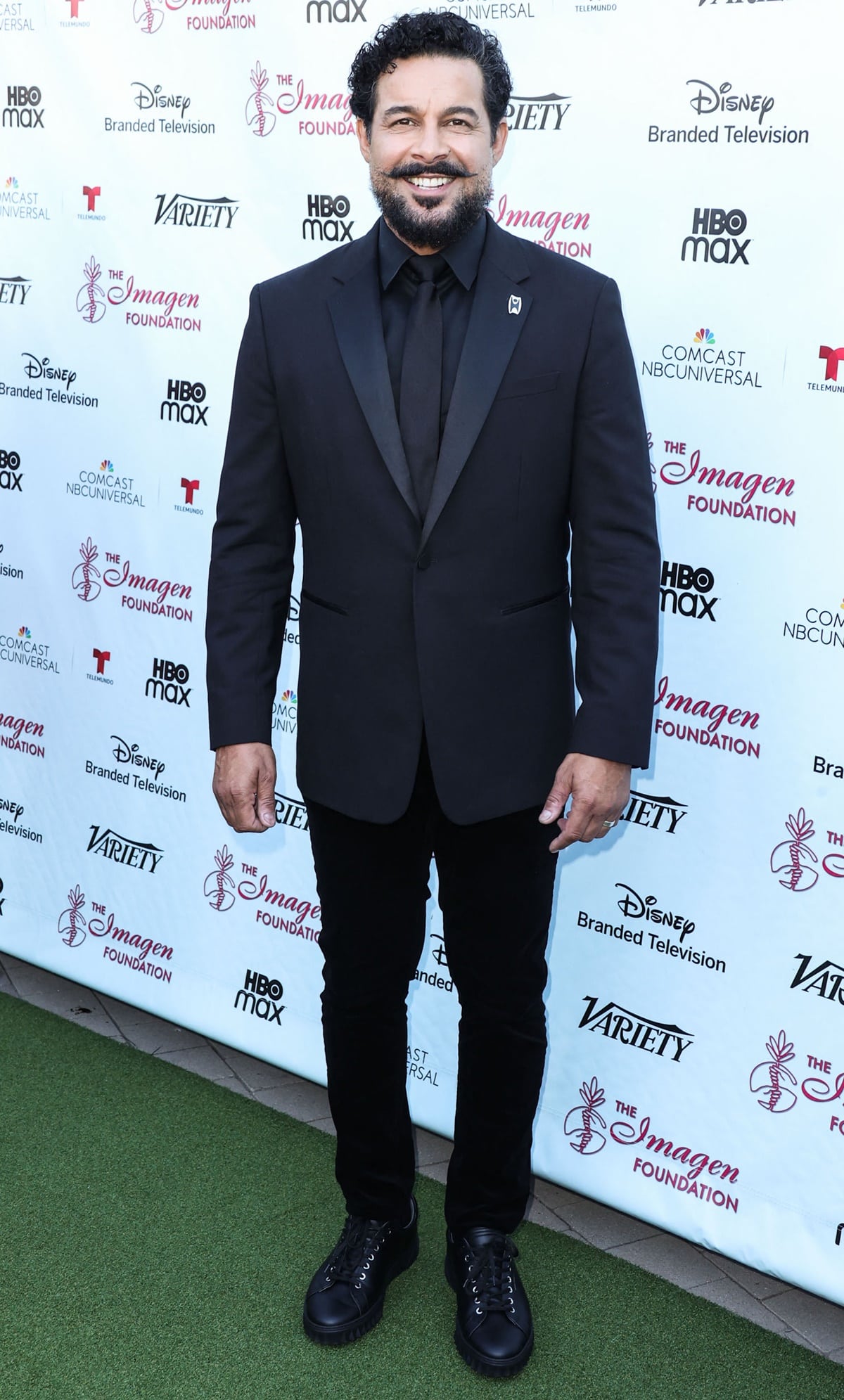 Jon Huertas attended the 2022 Imagen Awards at LA Plaza de Cultura y Artes on October 2, 2022, looking sharp in a classic black suit styled with a tonal dress shirt, skinny tie, and sleek black leather sneakers for a modern twist on formalwear