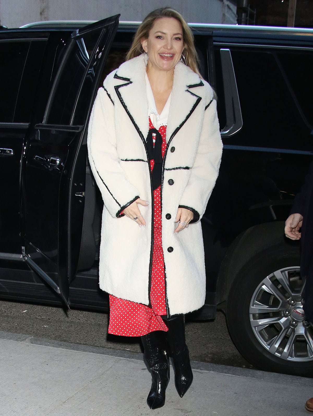 Kate Hudson arrived at The Today Show studios on December 14, 2022, pairing a retro red polka-dot Alessandra Rich dress and a white Maje faux-sheepskin coat with textured black knee-high boots by Alexandre Birman