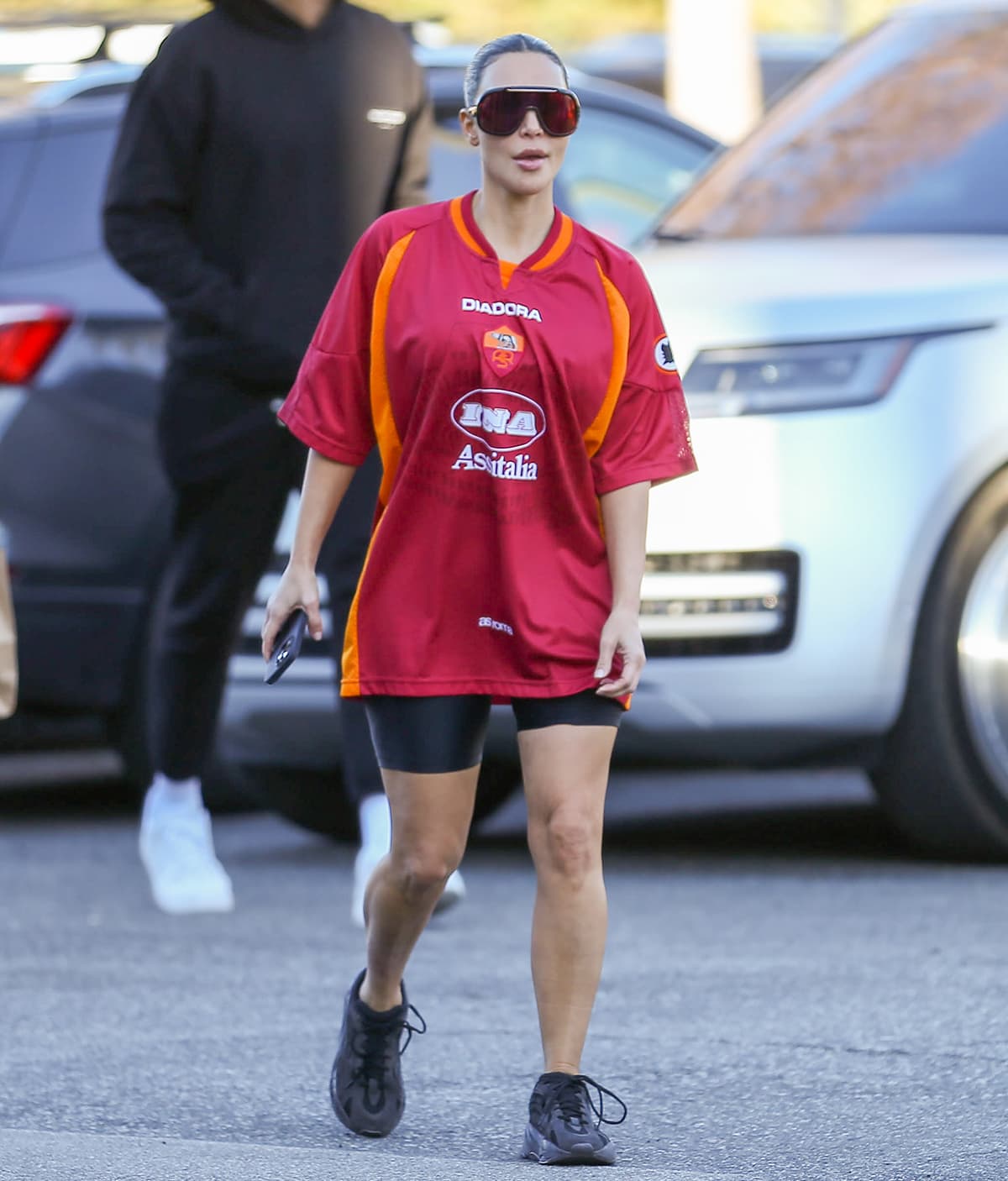 Kim Kardashian grounds her sporty courtside outfit with adidas Yeezy Boost 700 MNVN “Triple Black” sneakers, styled with biker shorts and a vintage Roma x Diadora jersey