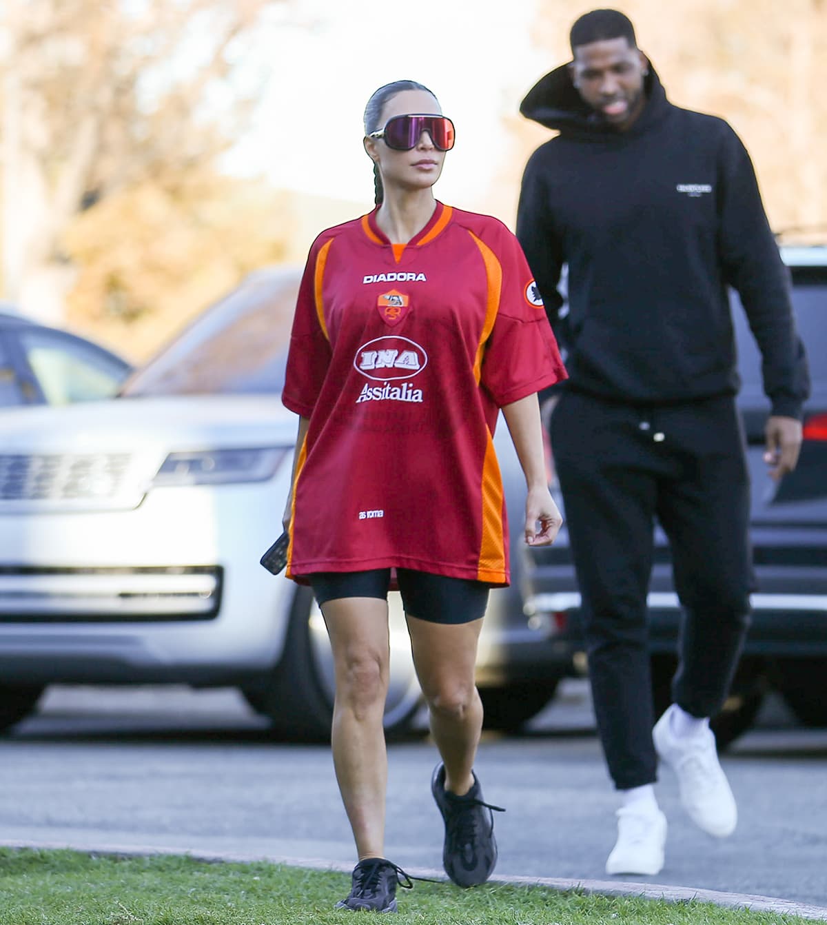Kim Kardashian pairs a vintage Roma x Diadora jersey and biker shorts with black Yeezy Boost 700 “Triple Black” sneakers and oversized Carrera Epica 0Uc/W3 shield sunglasses as Tristan Thompson accompanies her to Saint and North West’s basketball game in Los Angeles on January 27, 2023