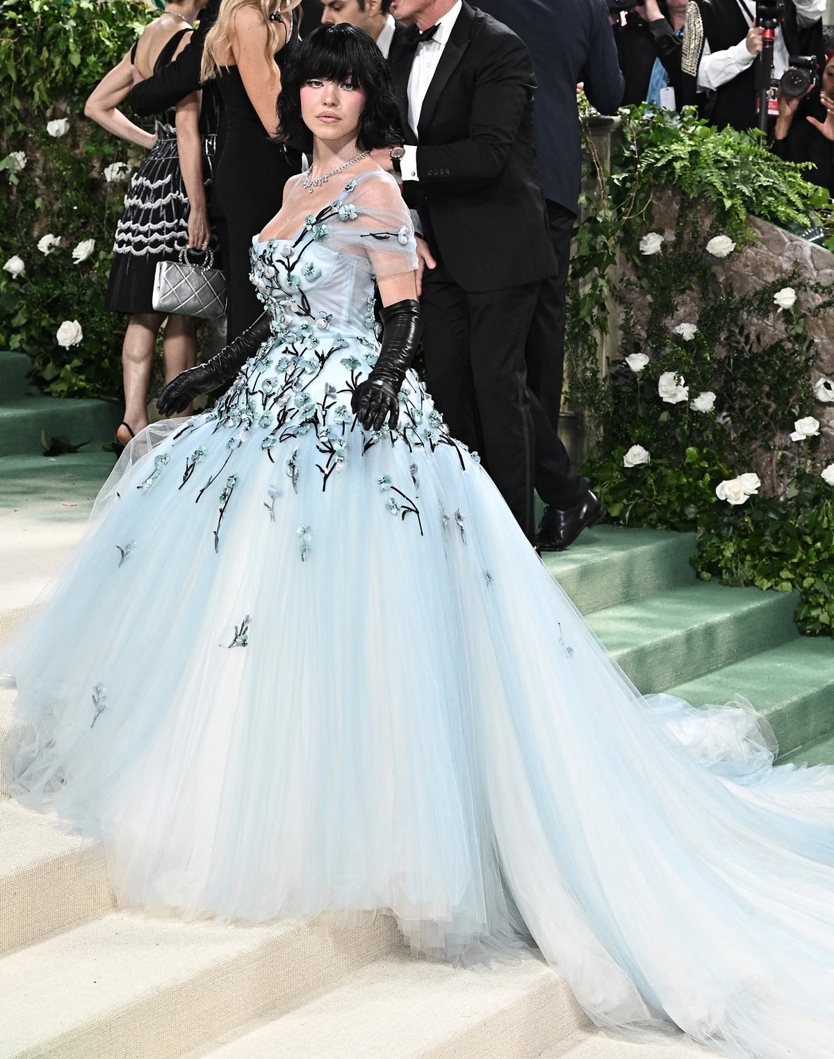 Sydney Sweeney transformed into a “dark enchanted princess” at the 2024 Met Gala, wearing a custom Miu Miu light blue tulle gown with floral appliqués, black opera gloves, and a jet-black bob wig