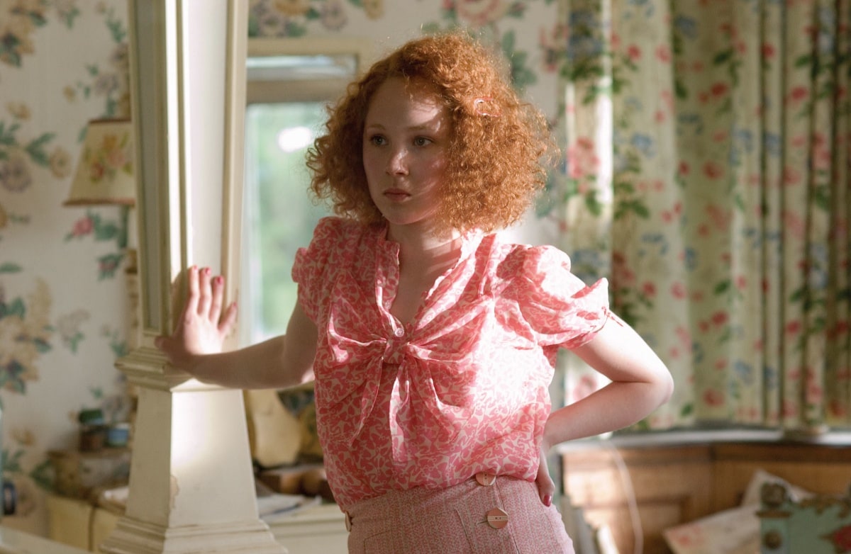 Juno Temple as Lola Quincey in Atonement (2007), wearing a vintage-inspired pink blouse and high-waisted slacks—her youthful, doll-like style masking the darker turn her character takes in the film’s emotional narrative