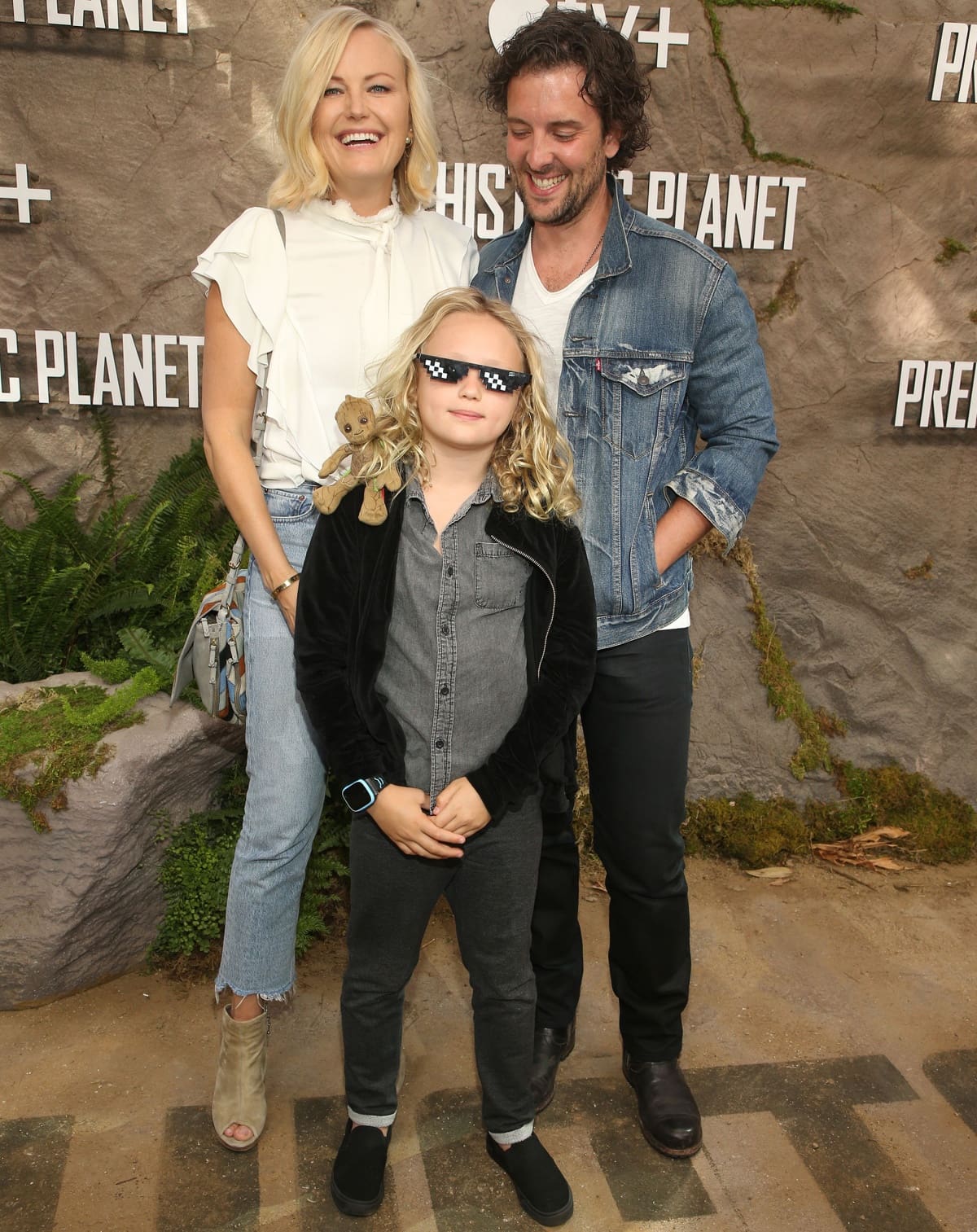 Malin Akerman radiates effortless chic at the Prehistoric Planet premiere in Los Angeles on May 15, 2022, wearing a ruffled white blouse, distressed jeans, and taupe peep-toe booties, posing alongside her husband Jack Donnelly and son Sebastian, who adds a fun touch with pixelated sunglasses and casual sneakers