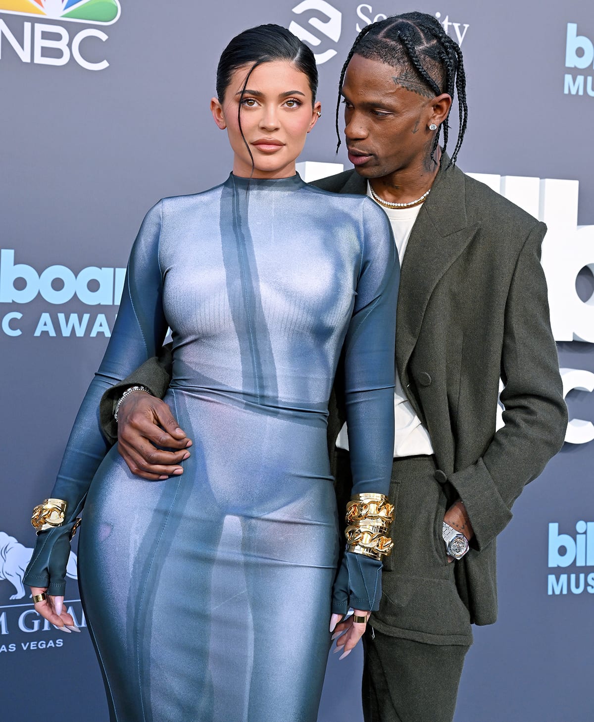 Kylie Jenner turns heads in a futuristic, figure-hugging Balmain bodycon gown with bold gold cuffs, posing alongside Travis Scott at the 2022 Billboard Music Awards
