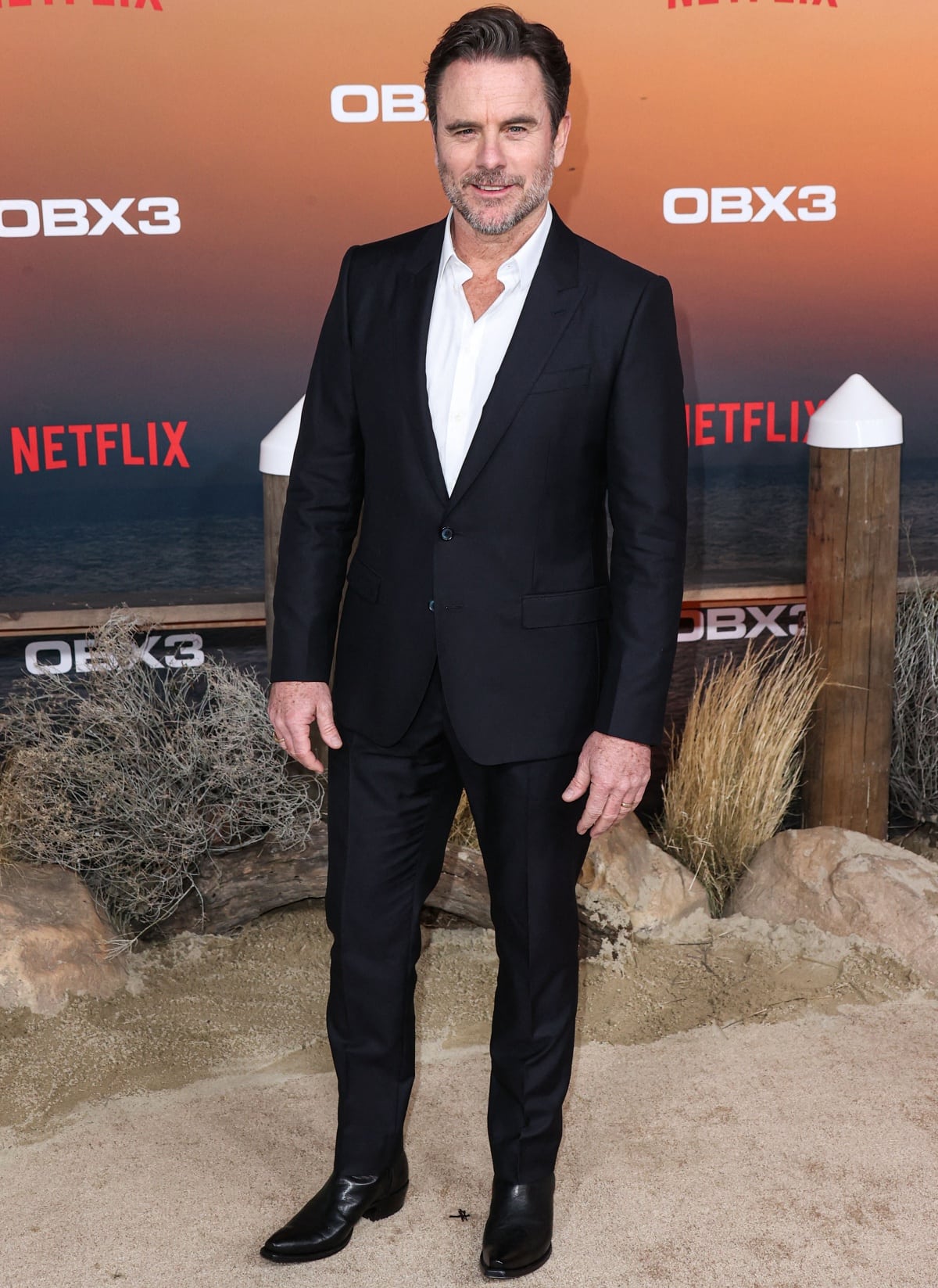 Charles Esten, who wears a US men’s size 11 shoe, looked sharp in a classic black tailored suit and white button-down shirt, finishing the look with sleek pointed-toe leather boots at the premiere of Netflix’s Outer Banks Season 3.
