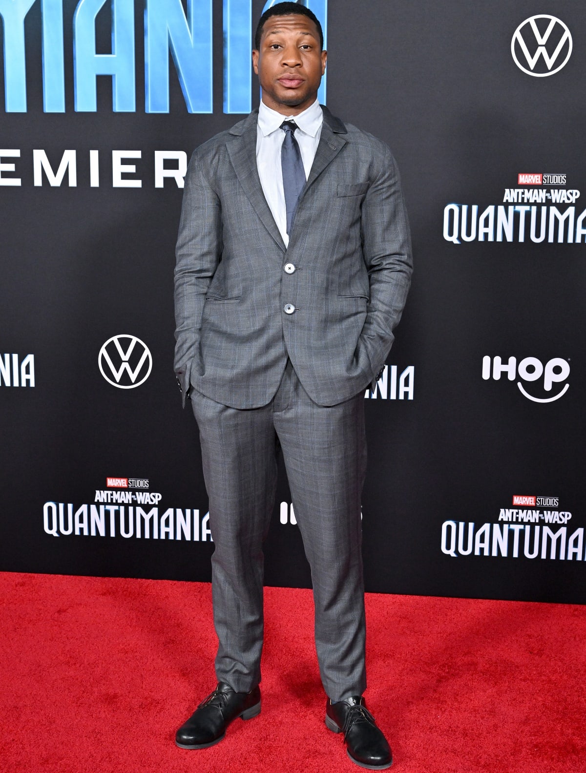 Jonathan Majors exuded understated sophistication in a tailored gray suit, crisp shirt, and tie, grounding the look with sleek black leather dress shoes for a refined Marvel red-carpet moment