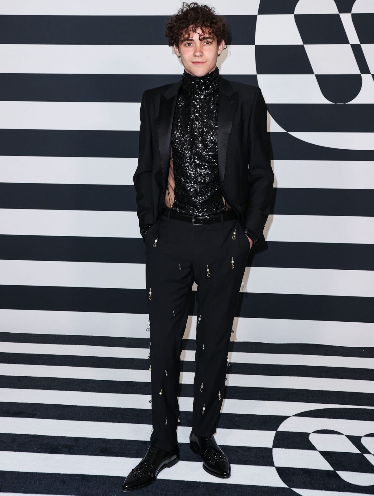 Joshua Bassett attending the Warner Music Group’s pre-Grammy party at The Hollywood Athletic Club in Los Angeles on February 3, 2023, wearing a black sequined turtleneck, tailored blazer, embellished trousers, and polished black dress shoes