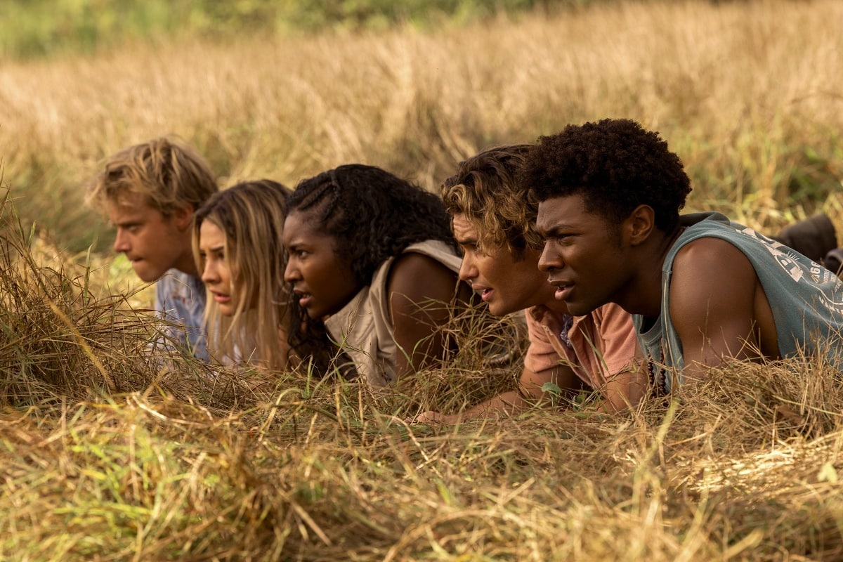 The Pogues—John B, Sarah, Cleo, JJ, and Pope—crawl through tall grass on a high-stakes mission, blending danger, loyalty, and suspense in true Pogue fashion