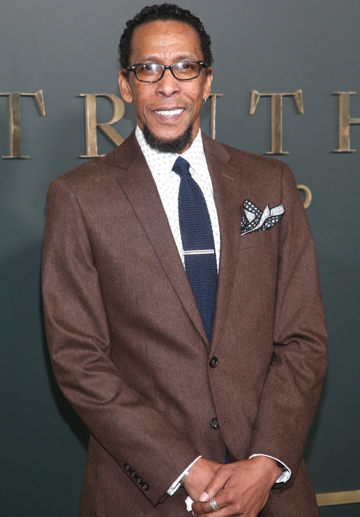 Ron Cephas Jones brought classic sophistication to the Truth Be Told premiere at the Samuel Goldwyn Theater in Los Angeles on November 11, 2019, wearing a tailored brown suit styled with a patterned dress shirt, navy knit tie, and a coordinating pocket square