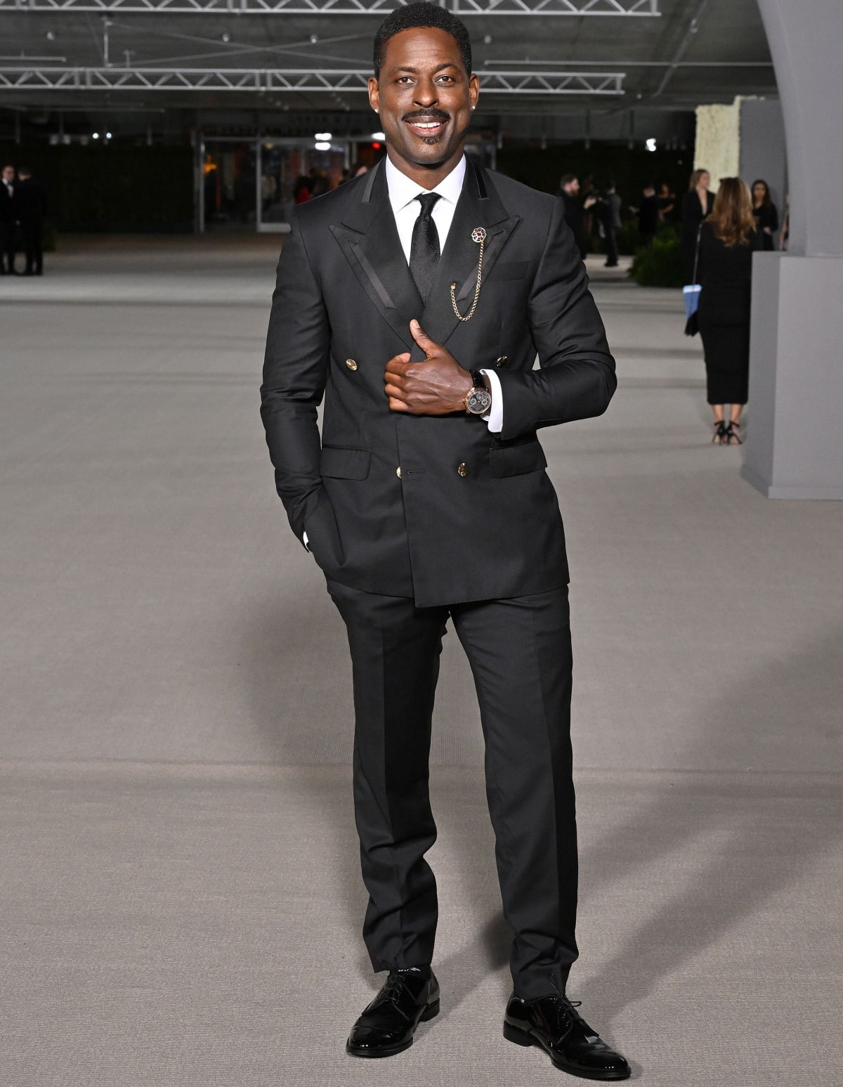 Sterling K. Brown attended the 2nd Annual Academy Museum Gala on October 16, 2022, in Los Angeles, exuding elegance in a double-breasted black suit, styled with glossy dress shoes, a satin tie, and a statement lapel chain for a refined red carpet look