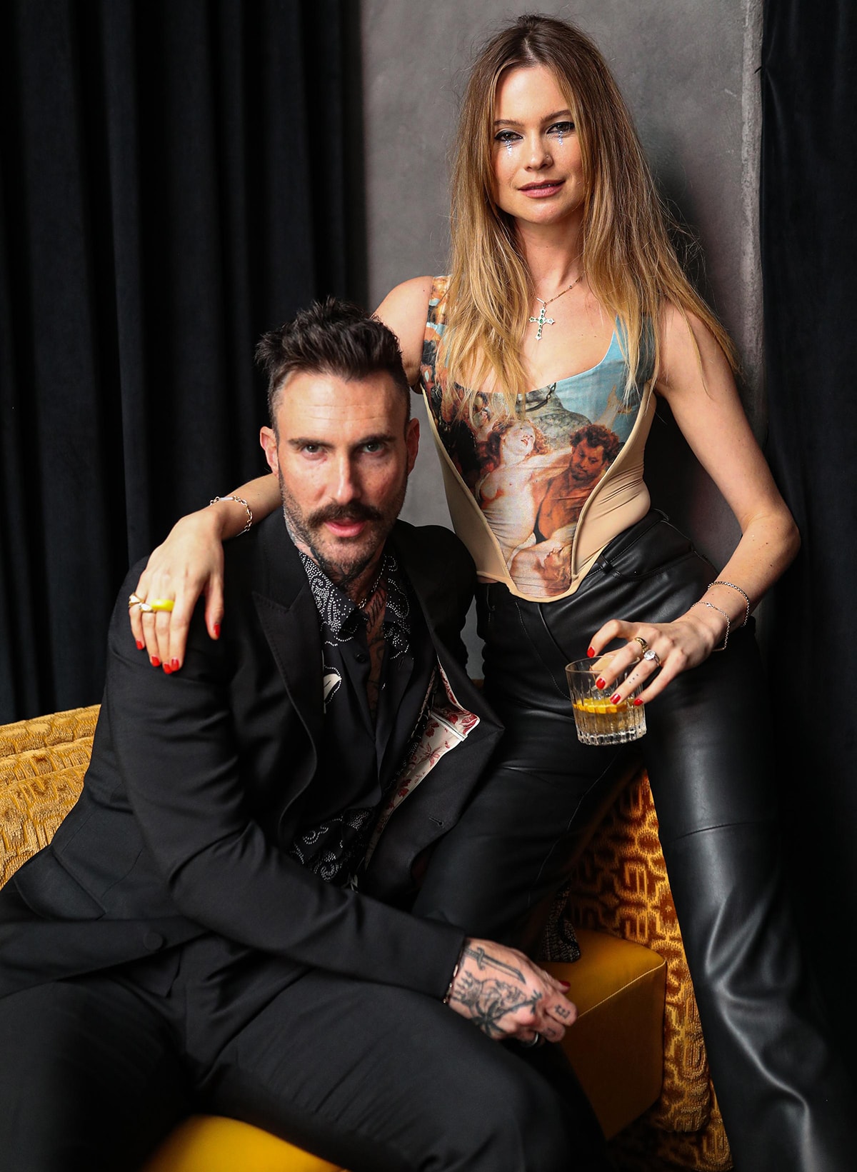 Adam Levine and Behati Prinsloo show off their edgy style, with Adam in a sleek black suit and Behati turning heads in a Renaissance-print corset top and leather pants