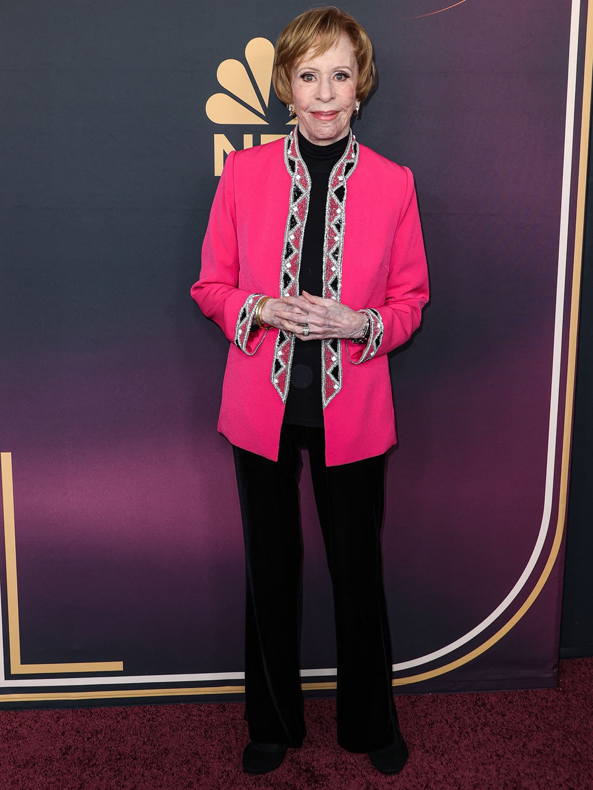 Carol Burnett brightens the red carpet in a vibrant hot pink embellished jacket, paired with classic black velvet pants and coordinating black shoes