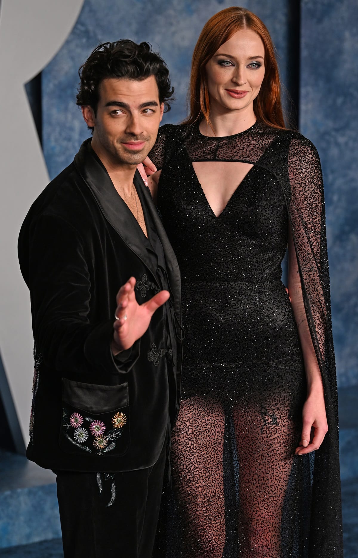 Sophie Turner’s Louis Vuitton gown combines a plunging cutout bodice with intricate black sequins and sheer cape sleeves, while Joe Jonas adds colorful floral embroidery to his black velvet Bode tailoring