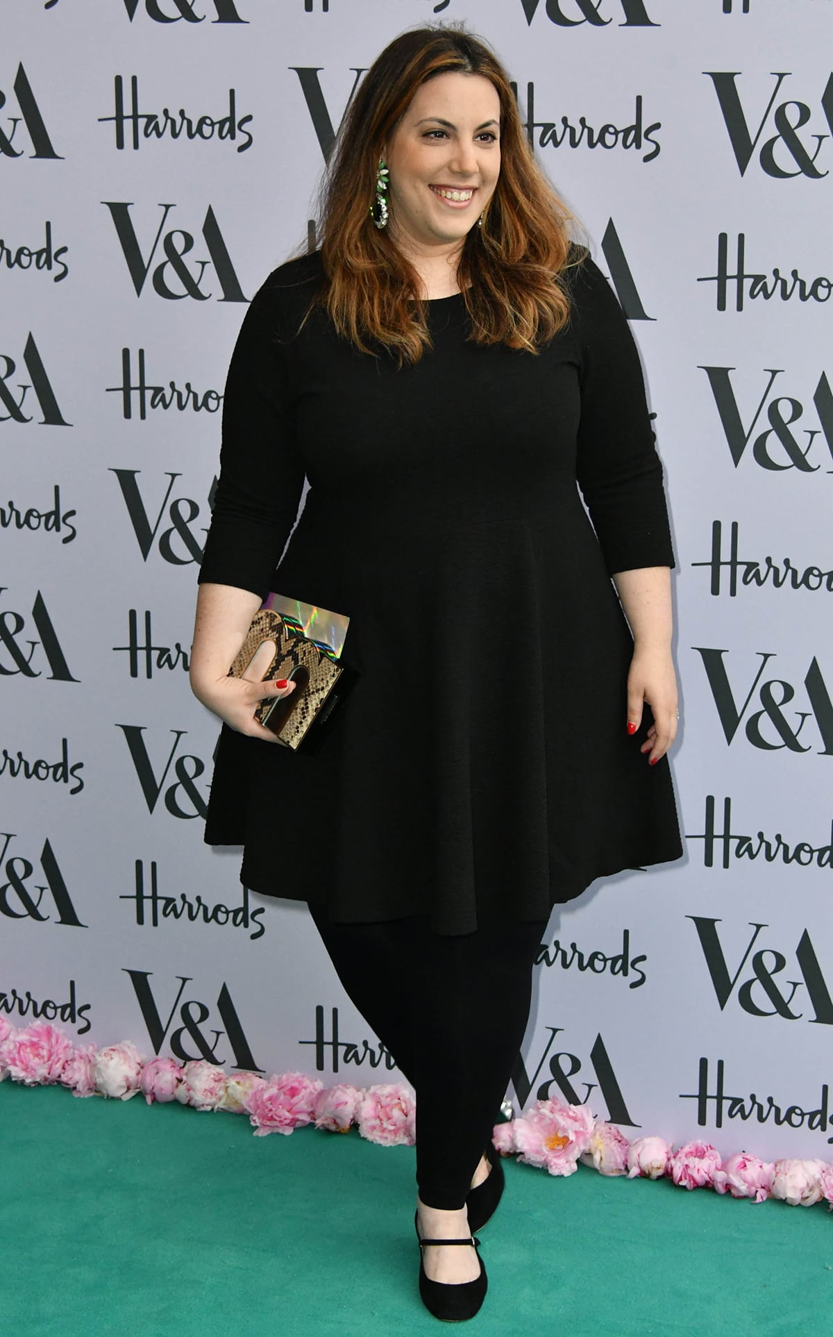 Mary Katrantzou exudes elegance in a chic black A-line dress, paired with classic Mary Jane shoes and a bold clutch at the VA Harrods event