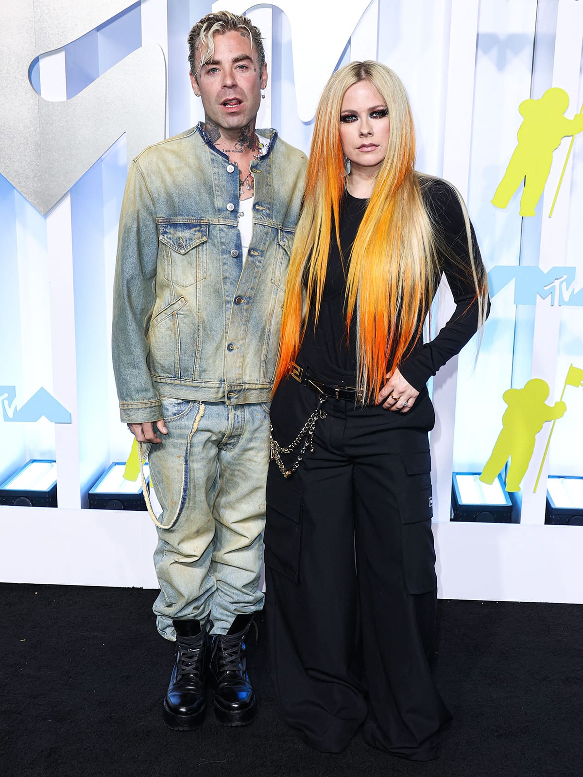Avril Lavigne channels her pop-punk roots in a sleek black cargo set and platform boots alongside Mod Sun, who paired distressed denim with lace-up combat boots, at the 2022 MTV VMAs in Newark, New Jersey
