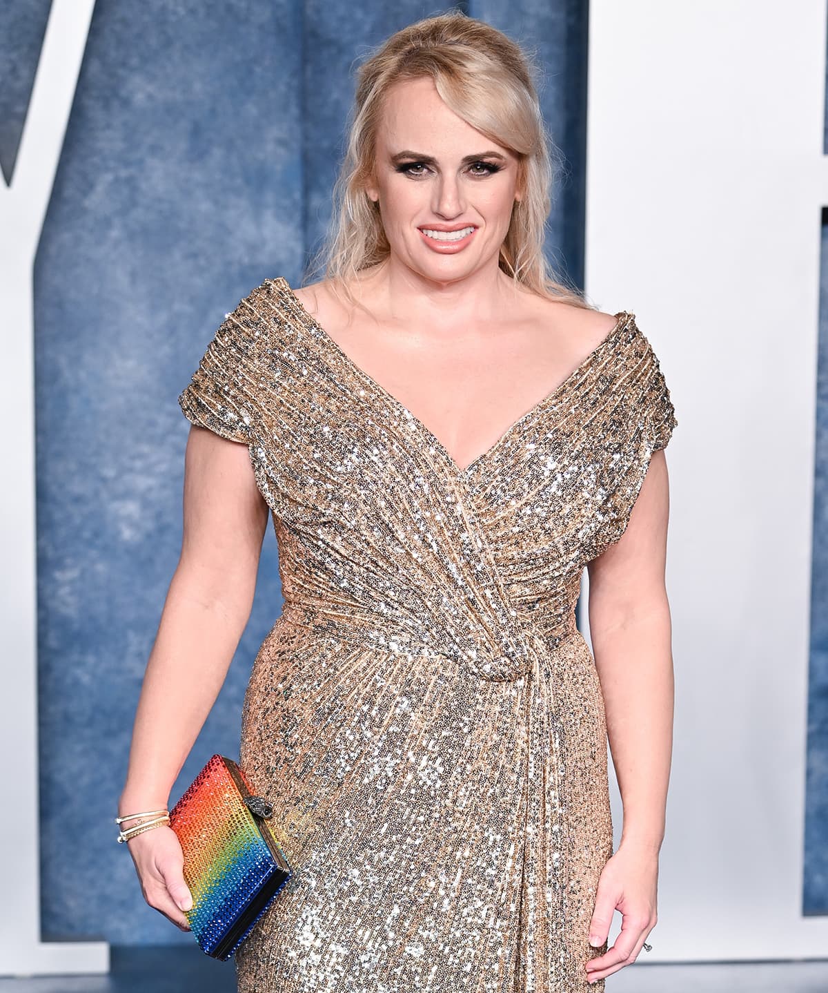 Rebel Wilson carries an LGBTQ-inspired rainbow clutch by Kurt Geiger and glams up with bronze smoky eyeshadow and pink lipstick