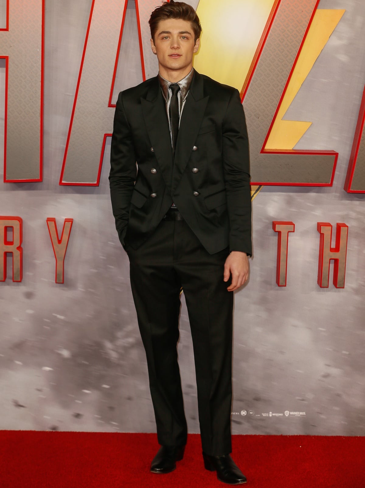 Asher Angel looked sharp at the Shazam! Fury of the Gods London premiere, wearing a sleek double-breasted black suit layered over a metallic silver shirt and tie, finished with polished black leather dress boots for a modern red-carpet edge