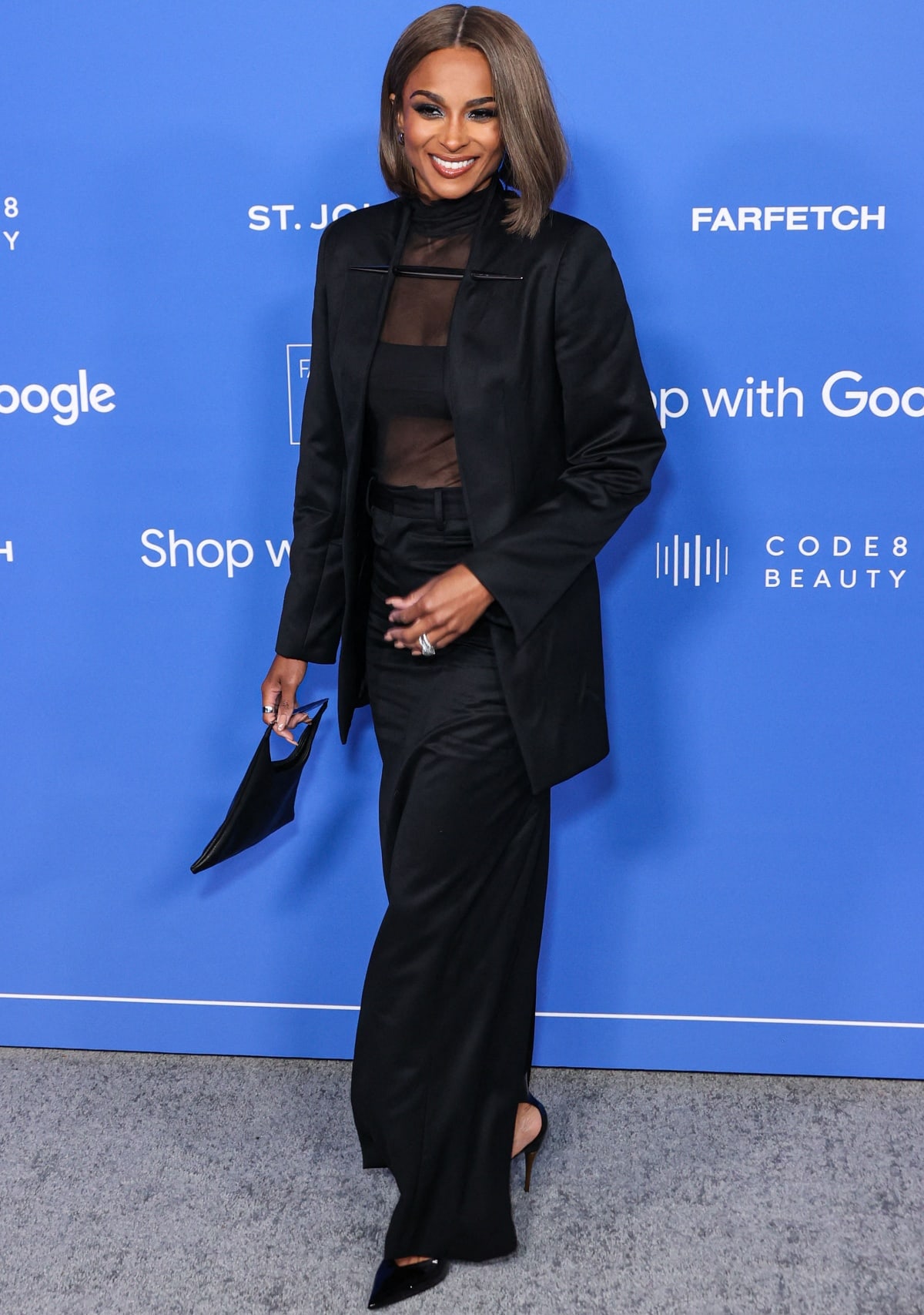Ciara donned a sophisticated Grace Ling ensemble, featuring a sheer black mesh turtleneck, a sleek bralette, a form-fitting Pillar skirt, and a Dagger Blazer, completed with pointy-toe heels and a black leather tote