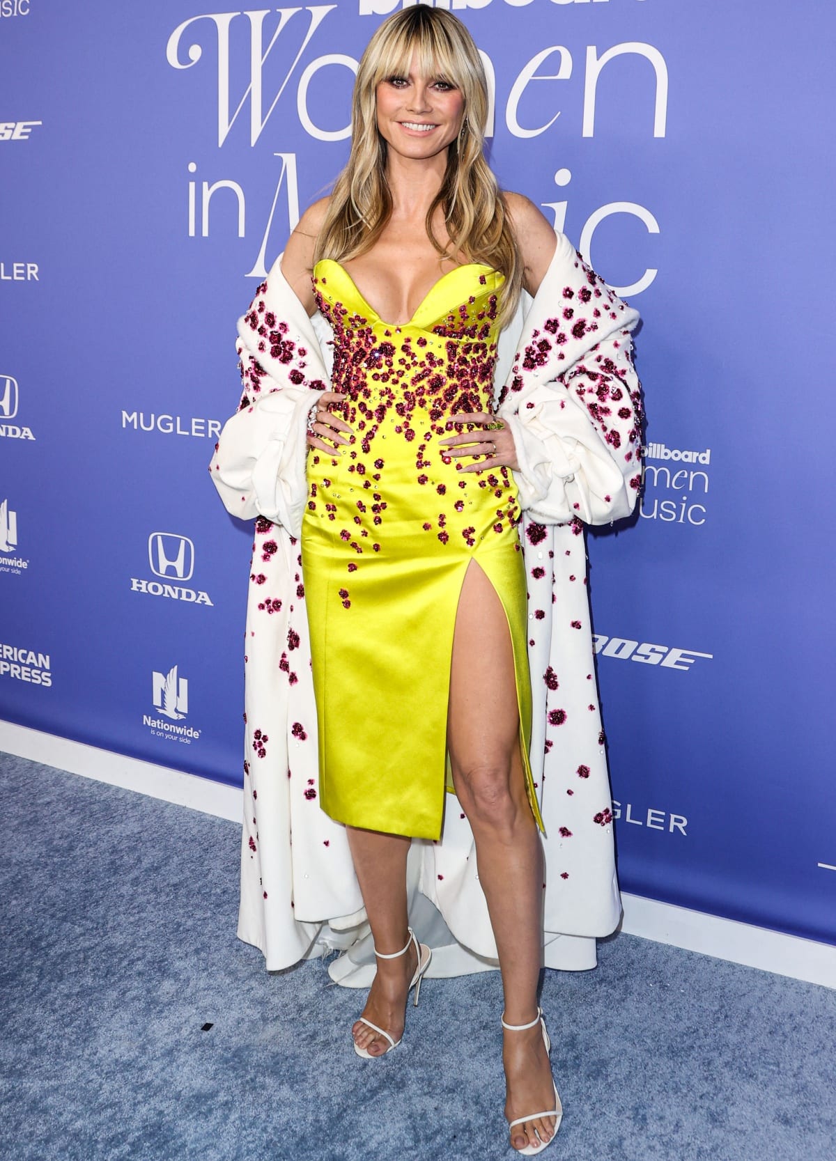 Heidi Klum turned heads in a vibrant yellow Miss Sohee Spring 2023 gown adorned with sparkling red embellishments, paired with elegant white ankle-strap heels