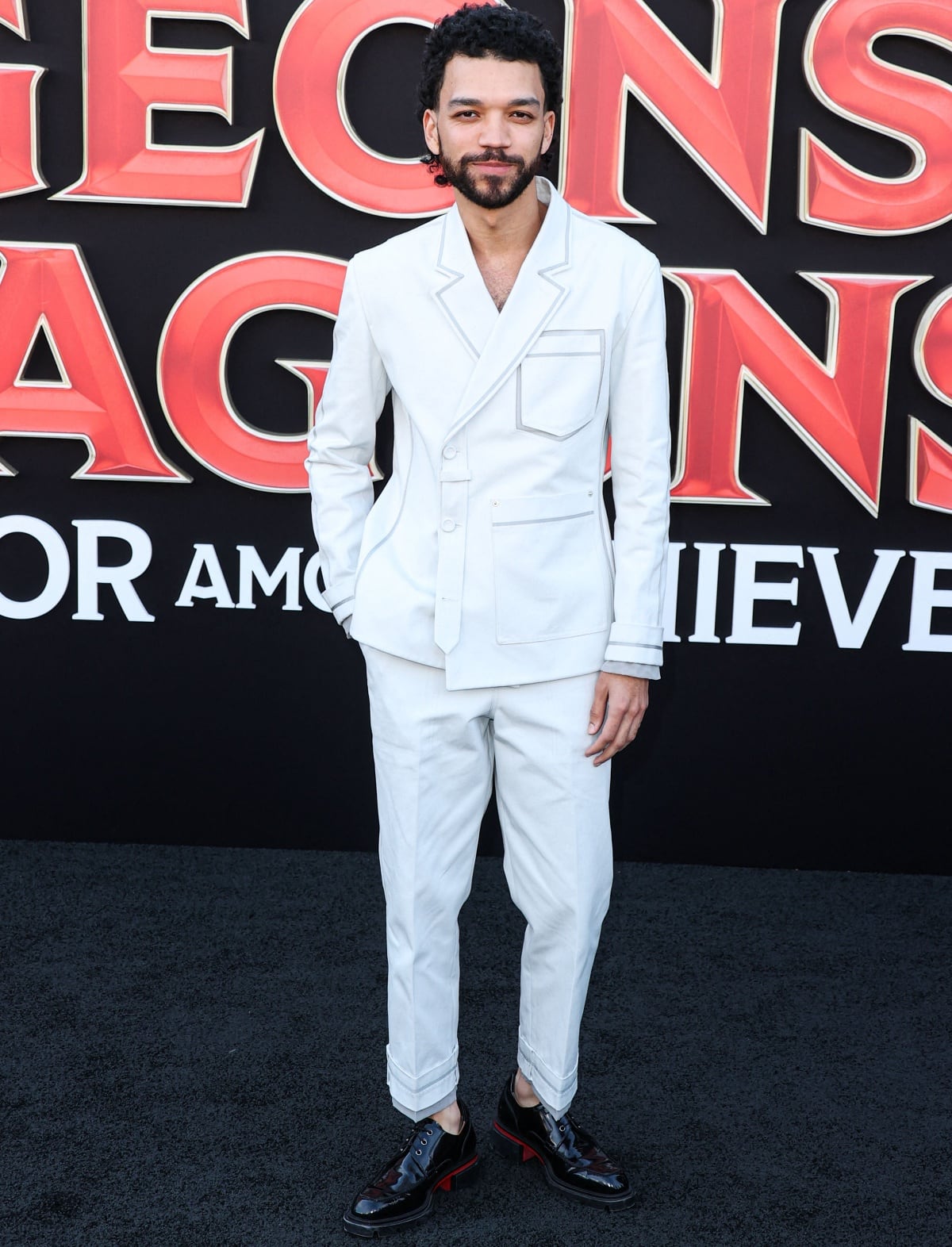 Justice Smith embraces minimalist elegance in a crisp white tailored suit with cuffed trousers and glossy black dress shoes, serving sharp monochrome sophistication at the Dungeons Dragons: Honor Among Thieves Los Angeles premiere