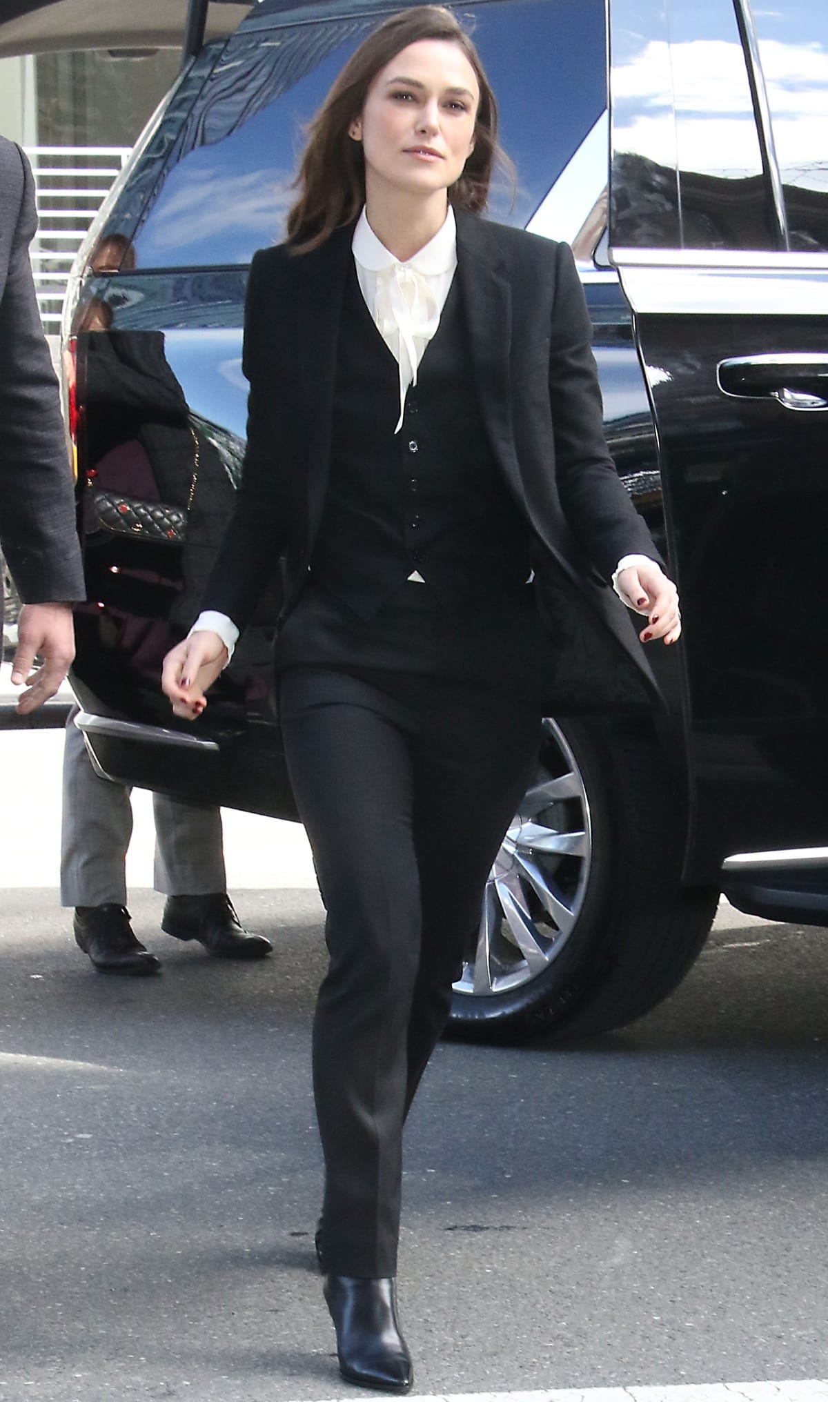 Keira Knightley cuts a sleek figure in a Celine three-piece black suit styled with a silk lavalliere blouse and pointed calfskin ankle boots for a refined take on Parisian power dressing