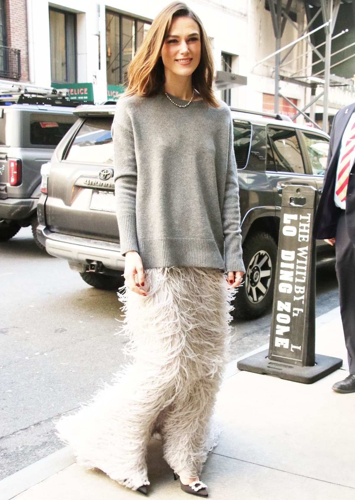 Keira Knightley softens her style in a Valentino Pre-Fall 2023 gray sweater and feather-trimmed maxi skirt, paired with Roger Vivier heels that add a romantic, textural finish