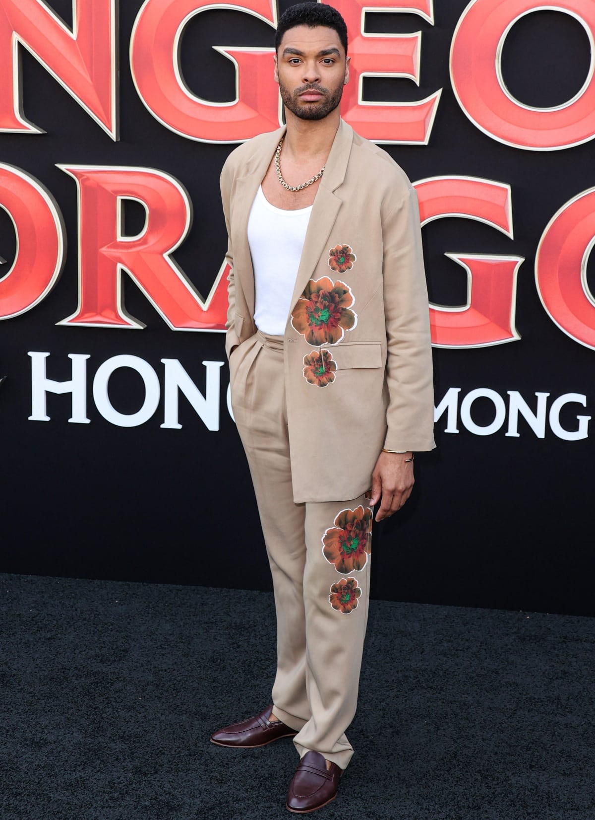 Regé-Jean Page exudes modern sophistication in a tan Love Hero suit adorned with hand-painted floral accents, styled with a white tank, gold chain, and brown Malone Souliers loafers at the Los Angeles premiere of Dungeons Dragons: Honor Among Thieves