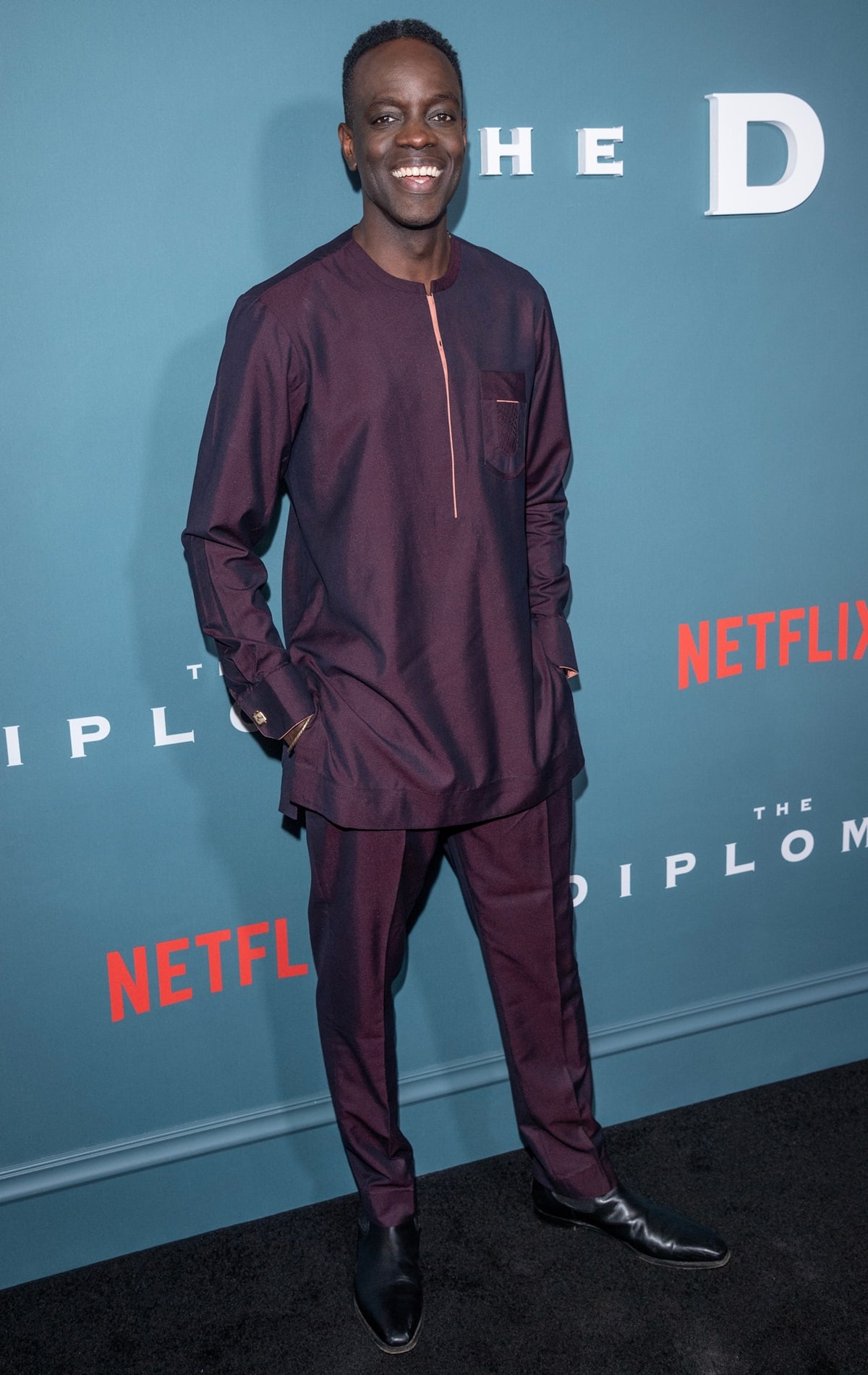 Ato Essandoh looks sharp in a burgundy traditional ensemble paired with sleek black leather dress shoes at The Diplomat premiere