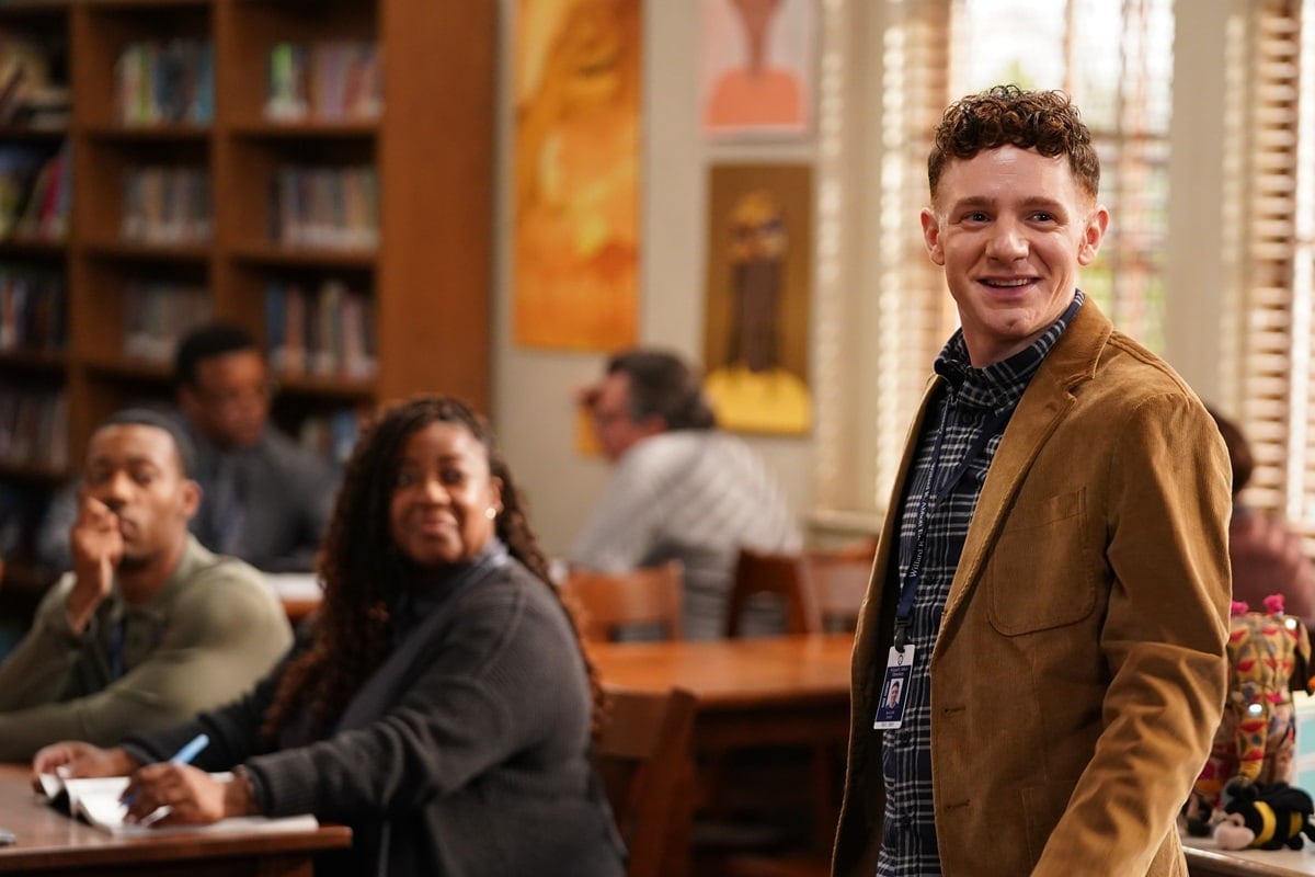 Chris Perfetti, who stands 5 feet 11 inches tall, embraces scholarly charm as history teacher Jacob Hill in a mustard corduroy blazer layered over a navy plaid shirt and school lanyard