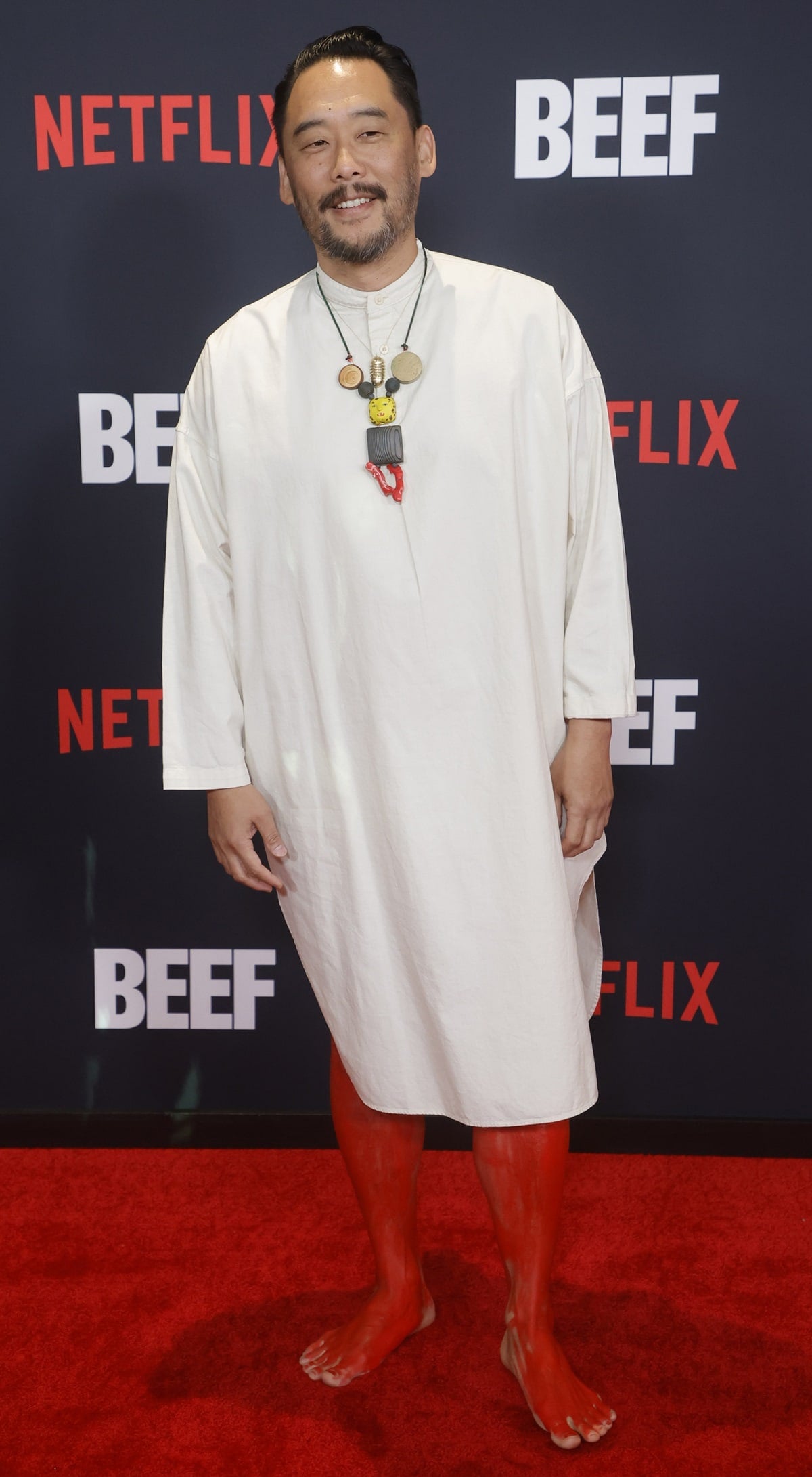 David Choe made a bold statement at the Beef premiere in a minimalist ivory tunic, eclectic sculptural necklace, and striking red body paint that extended down to his bare feet—eschewing shoes entirely