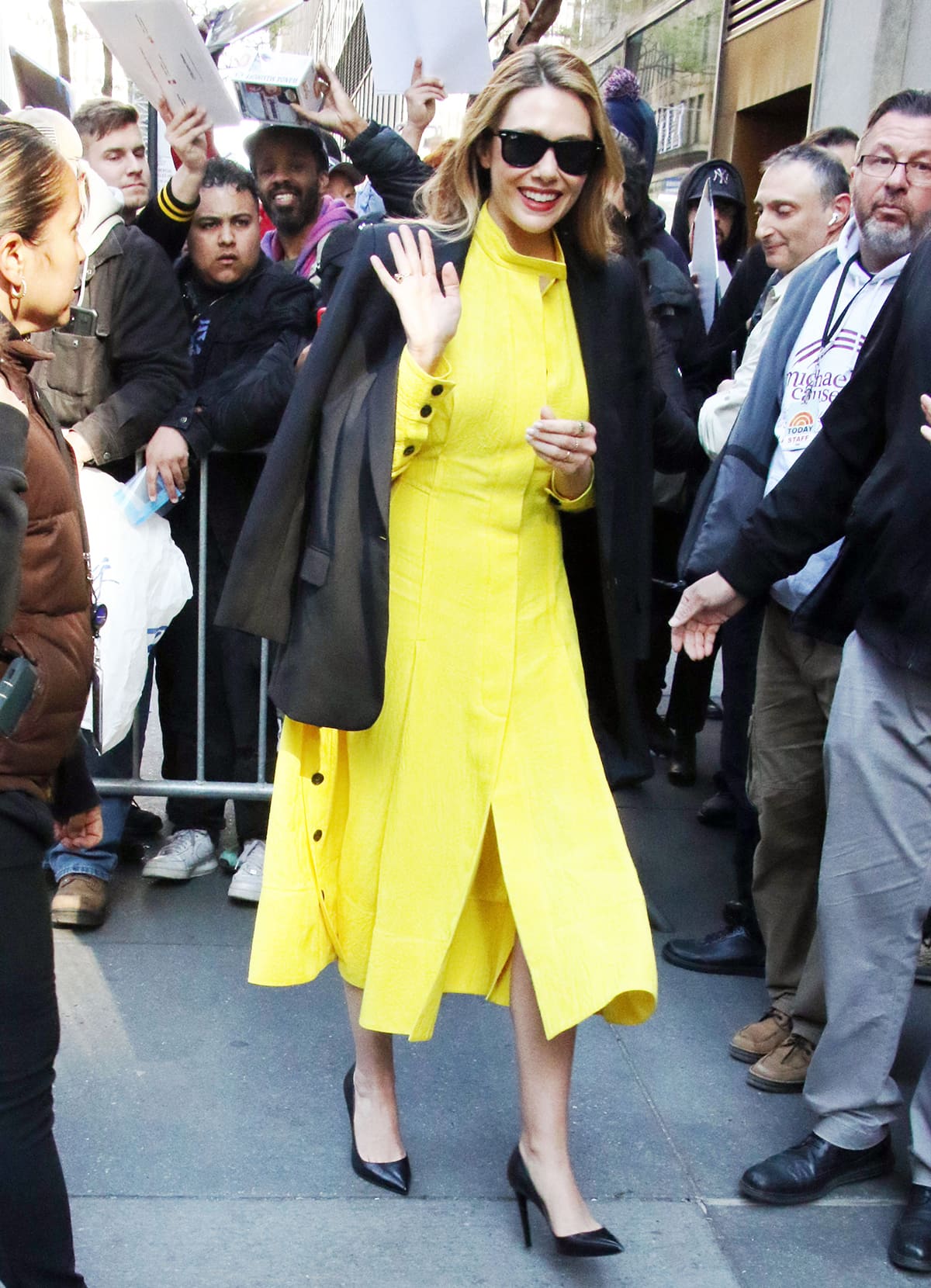 Elizabeth Olsen radiates springtime charm in a sunshine-yellow Proenza Schouler dress, layered with a black blazer and paired with sleek pointed-toe pumps and Ray-Ban Wayfarer sunglasses outside the Today show in New York City