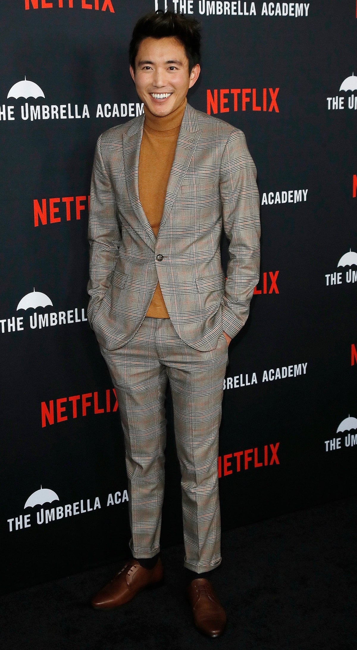 Justin H. Min brought classic charm to the red carpet in a tailored plaid suit, warm caramel turtleneck, and polished brown leather dress shoes