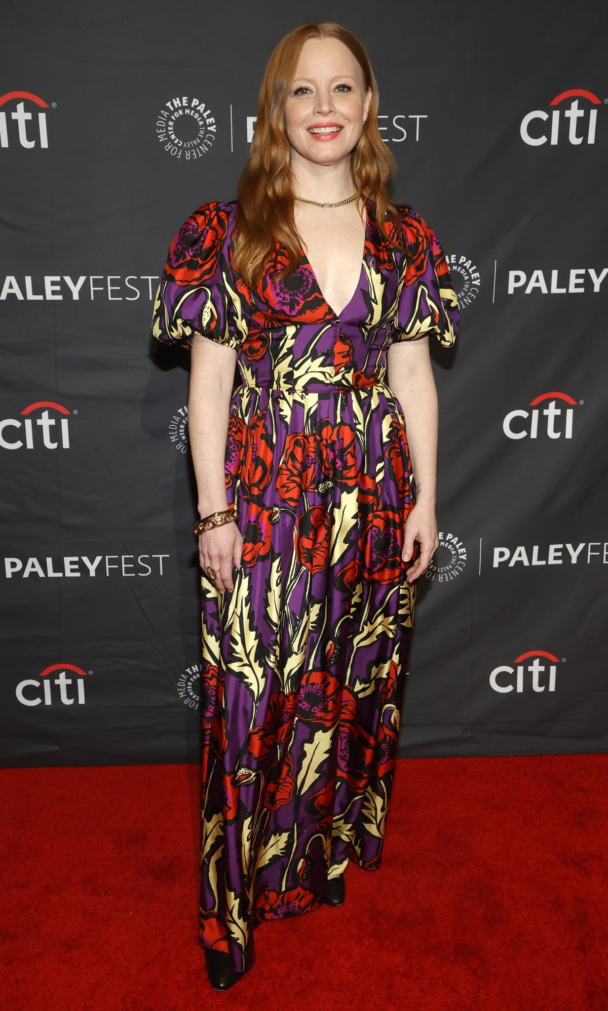 Lauren Ambrose lights up PaleyFest LA 2023 in a vibrant floral-print gown featuring puffed sleeves and bold red and purple hues, perfectly complemented by gold jewelry