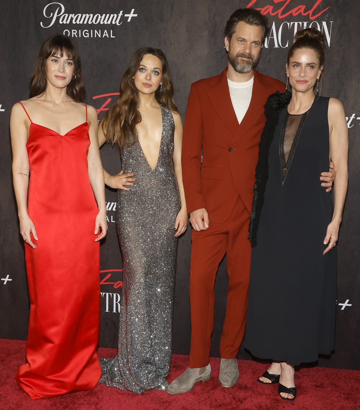 Lizzy Caplan stuns in a sleek red slip dress, Alyssa Jirrels dazzles in a shimmering silver gown, Joshua Jackson makes a bold statement in a rust-colored suit, and Amanda Peet looks chic in a black dress with statement ruffle details as they pose together at the Fatal Attraction premiere