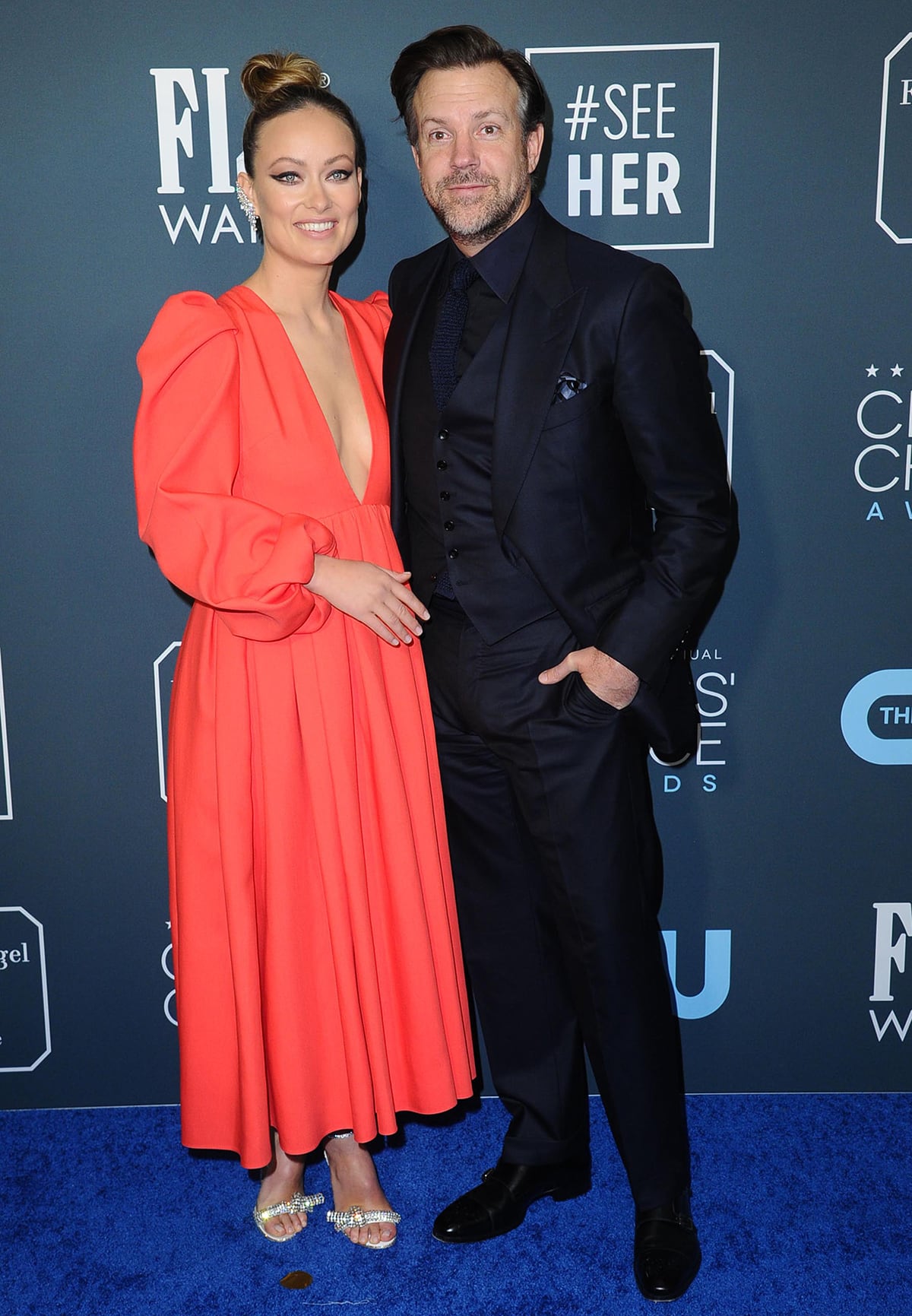 Olivia Wilde wore a coral Valentino Spring 2020 puff-sleeve midi dress, Messika Solena Maya earrings, and crystal-embellished Jimmy Choo Thyra sandals, while Jason Sudeikis complemented her look in a sharp navy three-piece suit as they posed together at the 2020 Critics’ Choice Awards