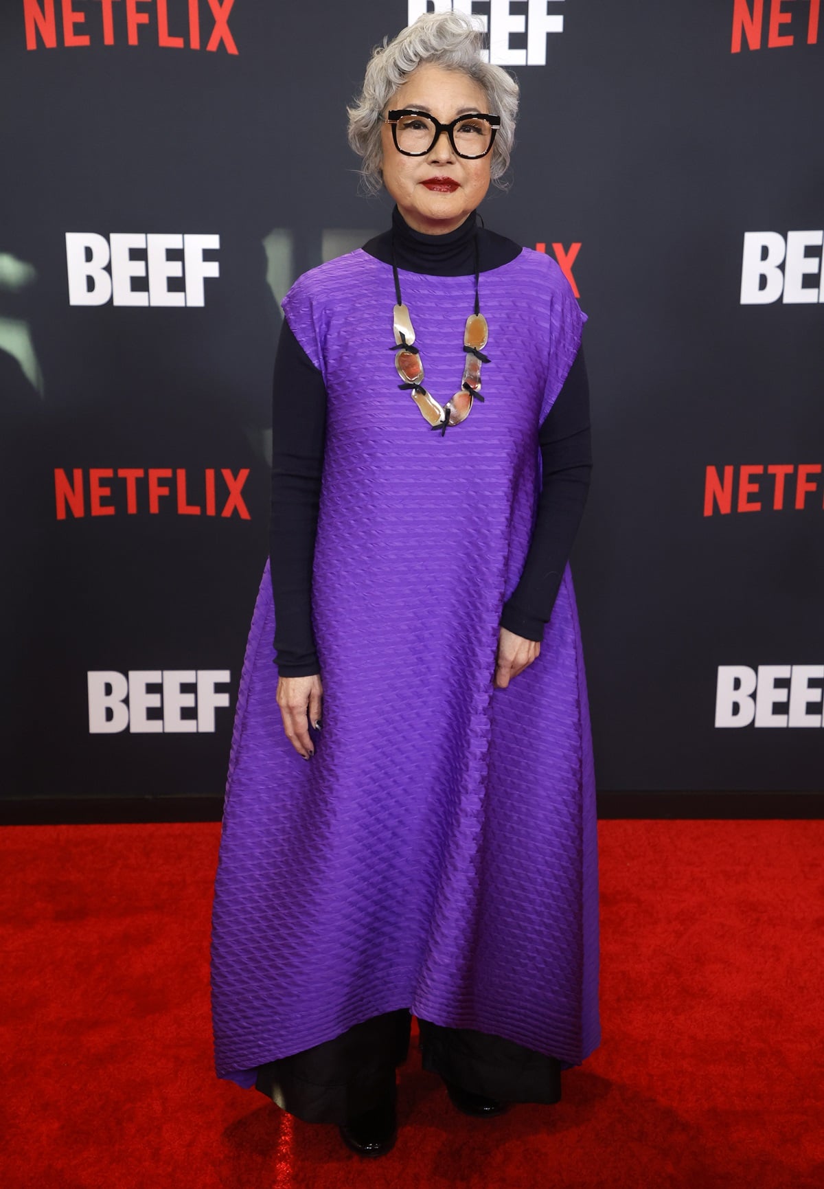 Patti Yasutake brought artistic elegance to the Beef premiere in a textured purple trapeze dress layered over a black turtleneck, paired with chunky black platform shoes and a sculptural statement necklace
