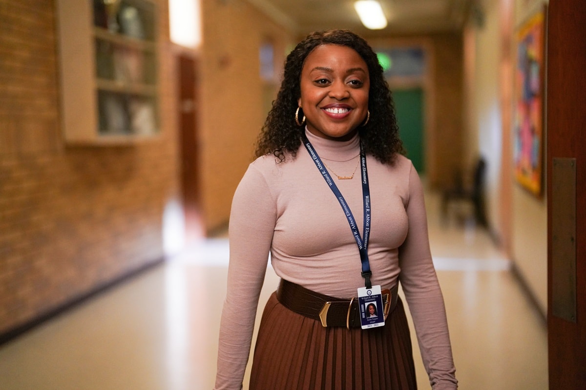 Quinta Brunson, the 4-foot-11 actress and creator of Abbott Elementary, exudes confidence in a fitted blush turtleneck, pleated brown midi skirt, and gold-accented belt during a scene from the hit series