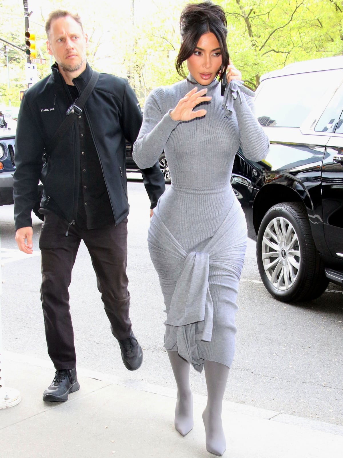 Kim Kardashian steps out in New York City wearing a body-hugging gray Alaïa silk and cashmere knit dress with a ribbed high neck, wraparound tie detail, and matching sock-style boots on April 26, 2023